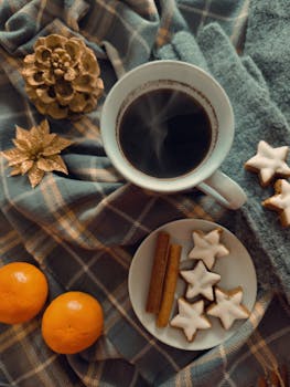 Warm winter setup with coffee, cinnamon, star cookies, oranges, and festive decor on plaid.