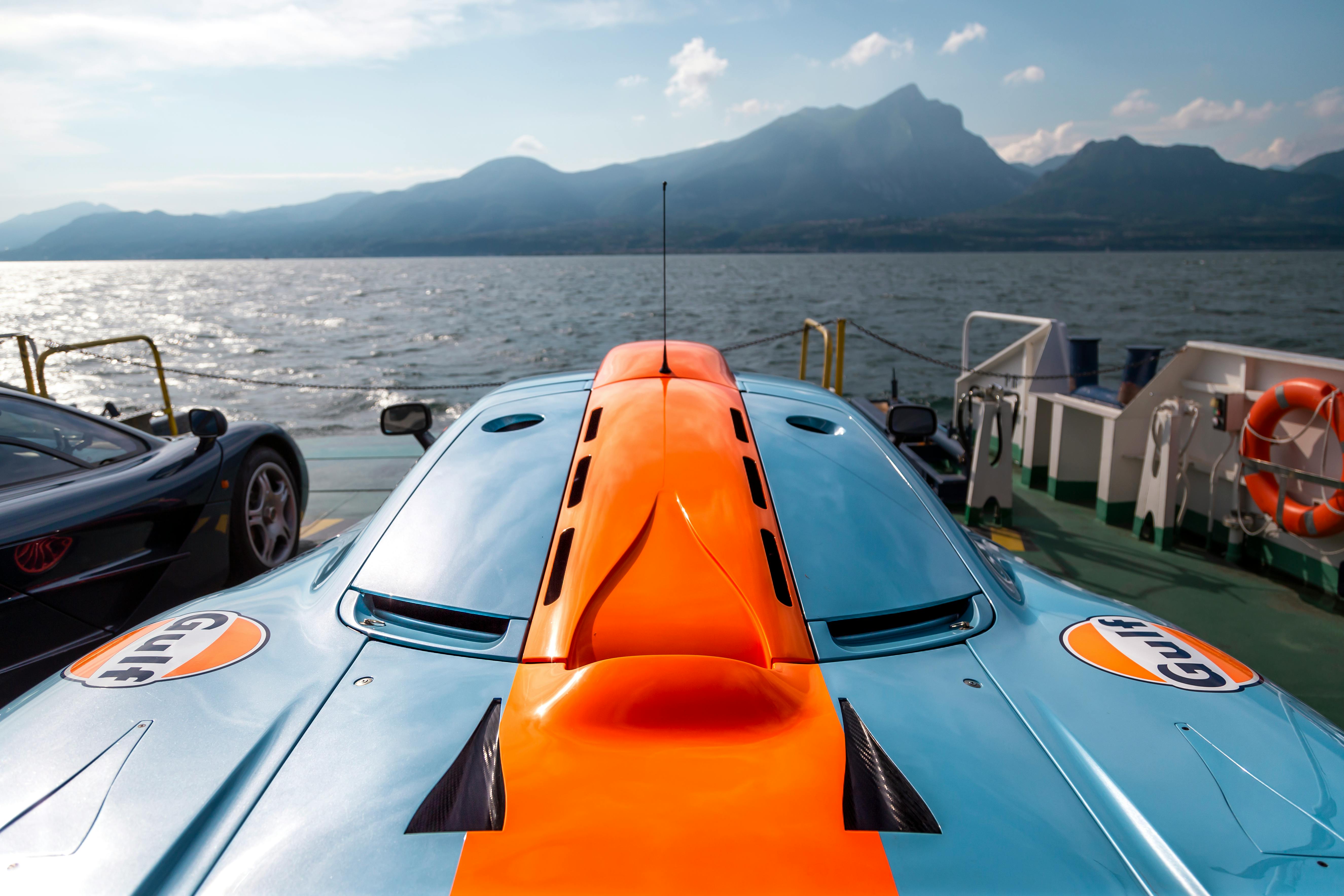 Close-up of a McLaren supercar aboard a ferry on Lake Garda with mountain backdrop.