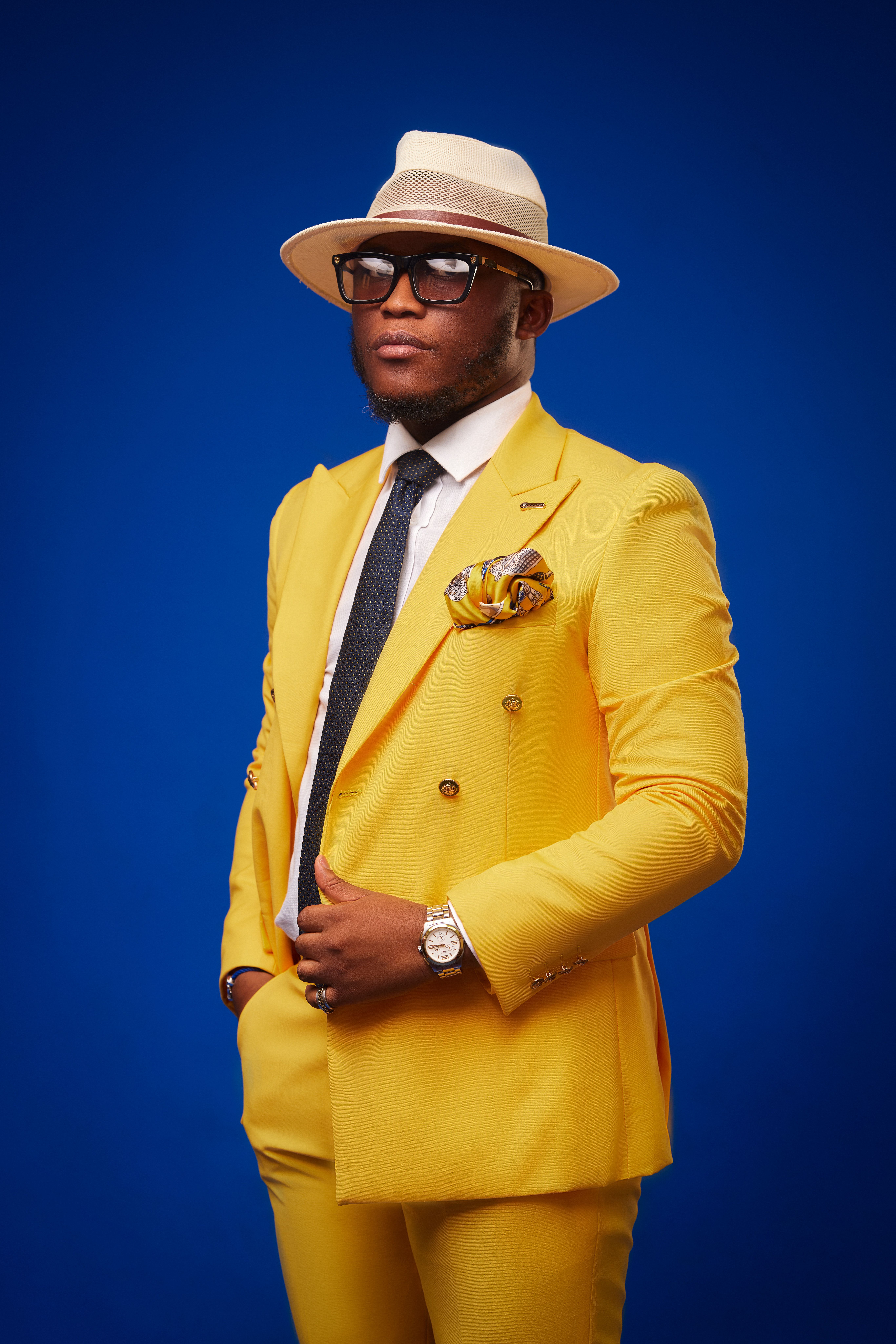 Fashionable gentleman in a vibrant yellow suit and hat against a blue background.