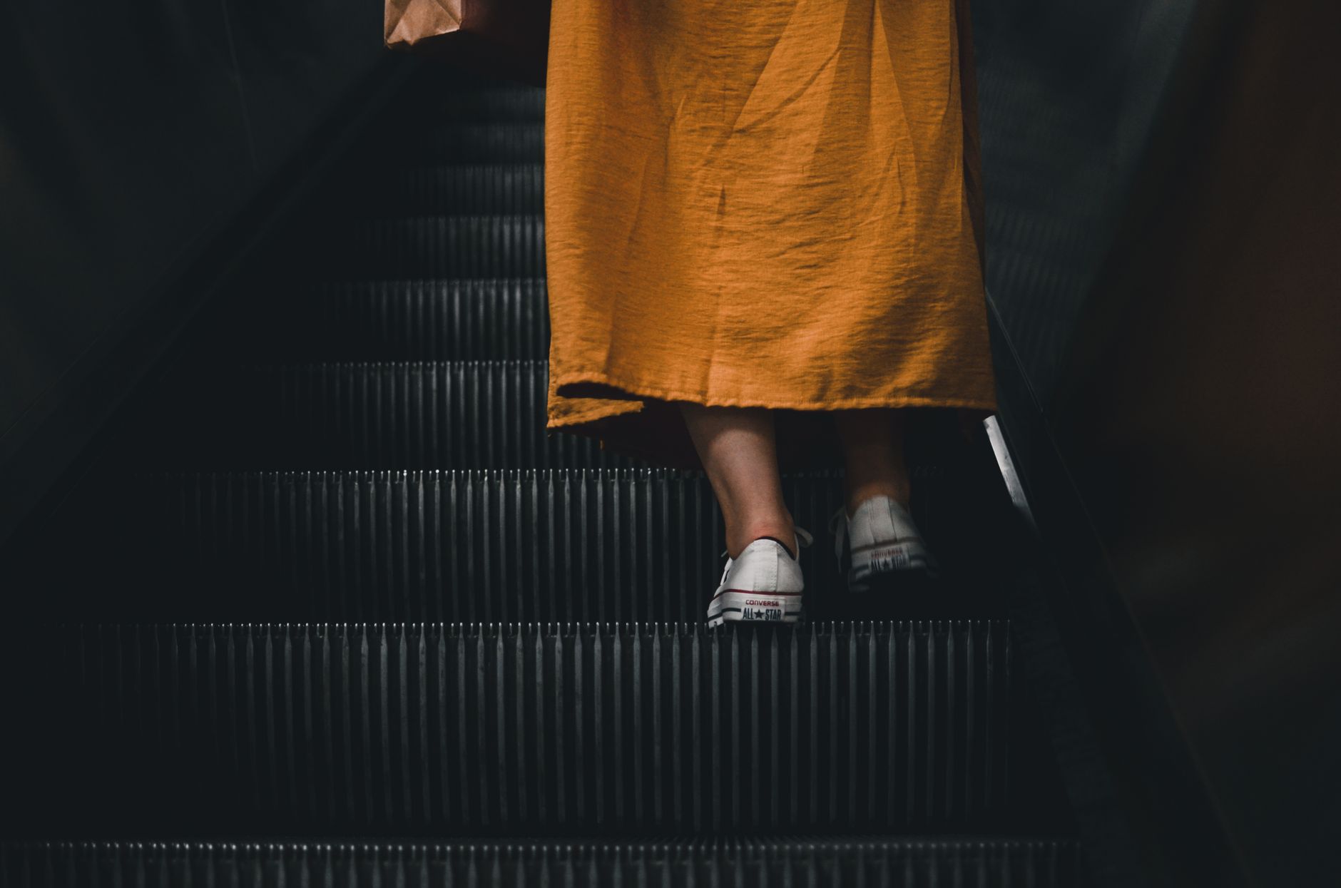 Woman in a yellow dress using an escalator in a dimly lit setting.