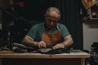 一位成年工匠穿着围裙，在室内的桌旁专注工作，周围摆放着工具