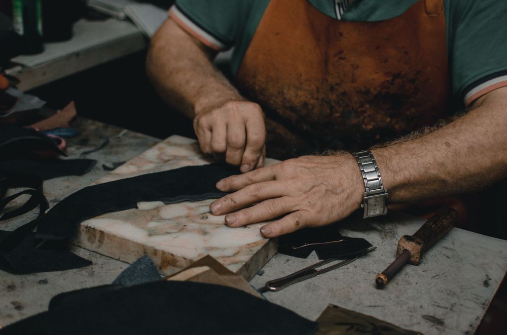 Mains d'un artisan travaillant une pièce de cuir sur l'établi.
