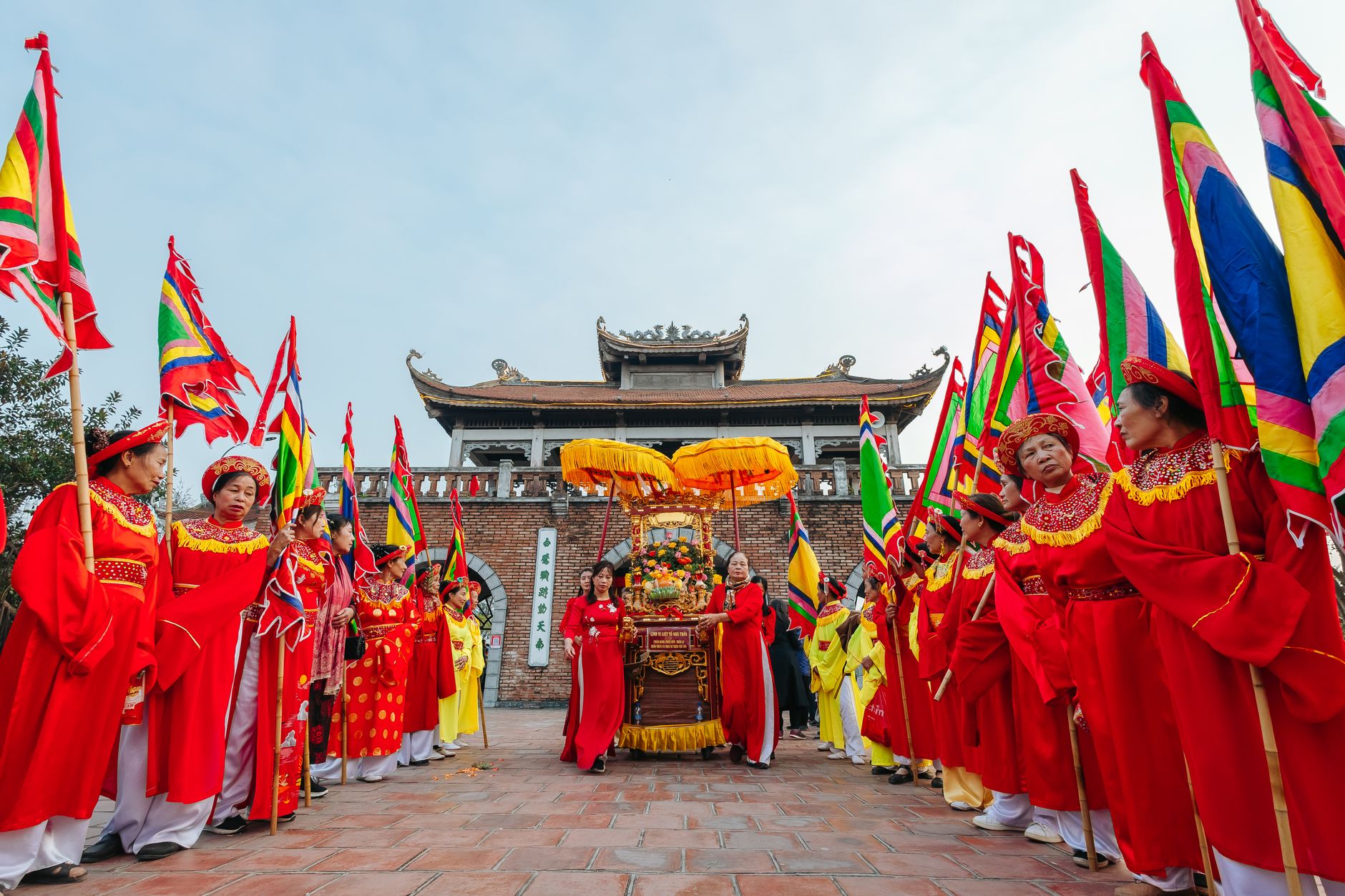 A vibrant traditional Vietnamese festival procession with colorful flags and participants in red costumes.