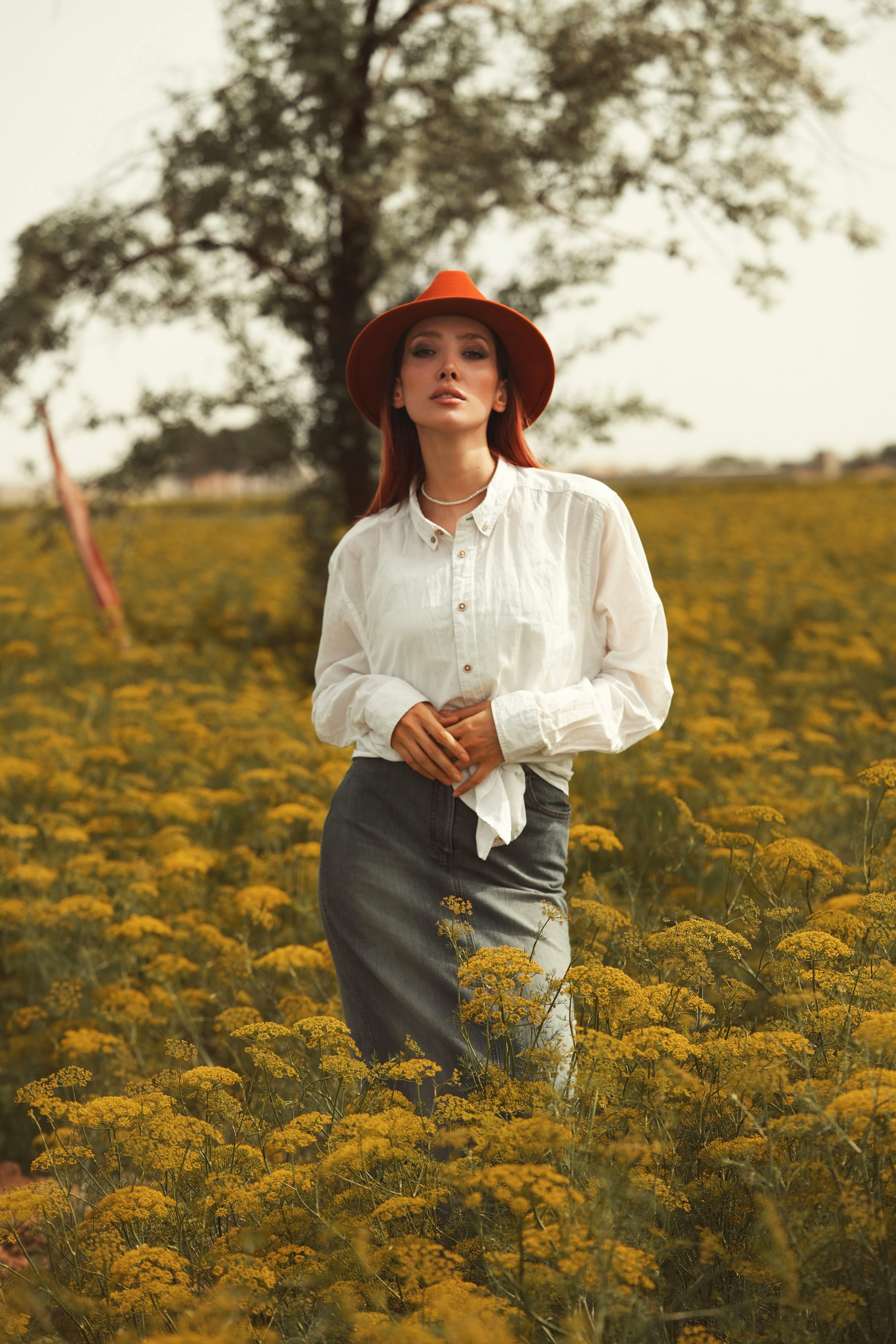 Woman in a field of yellow flowers wearing a stylish hat and white blouse, embodying elegance.