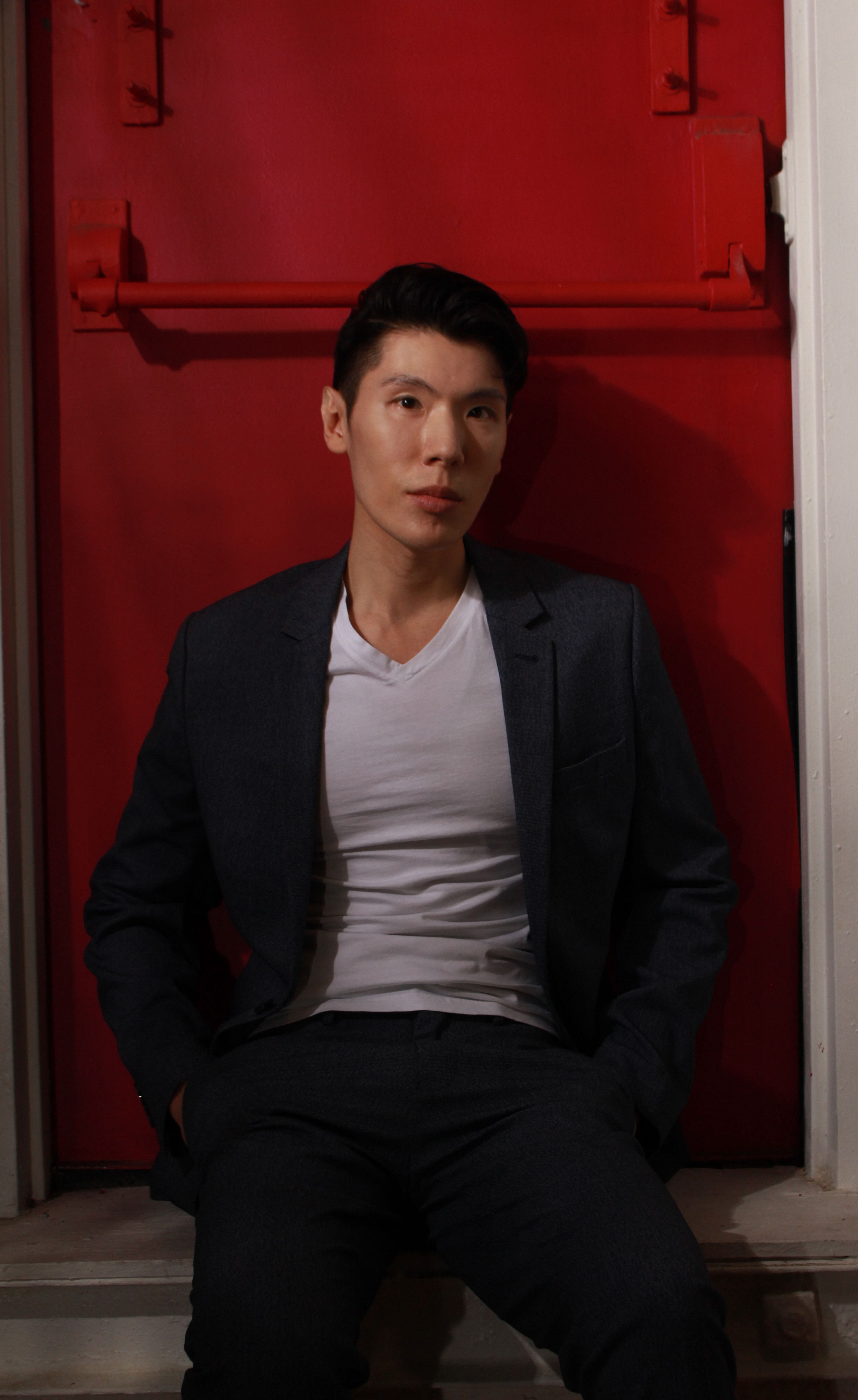 Stylish man in a suit sits in front of a vibrant red door.