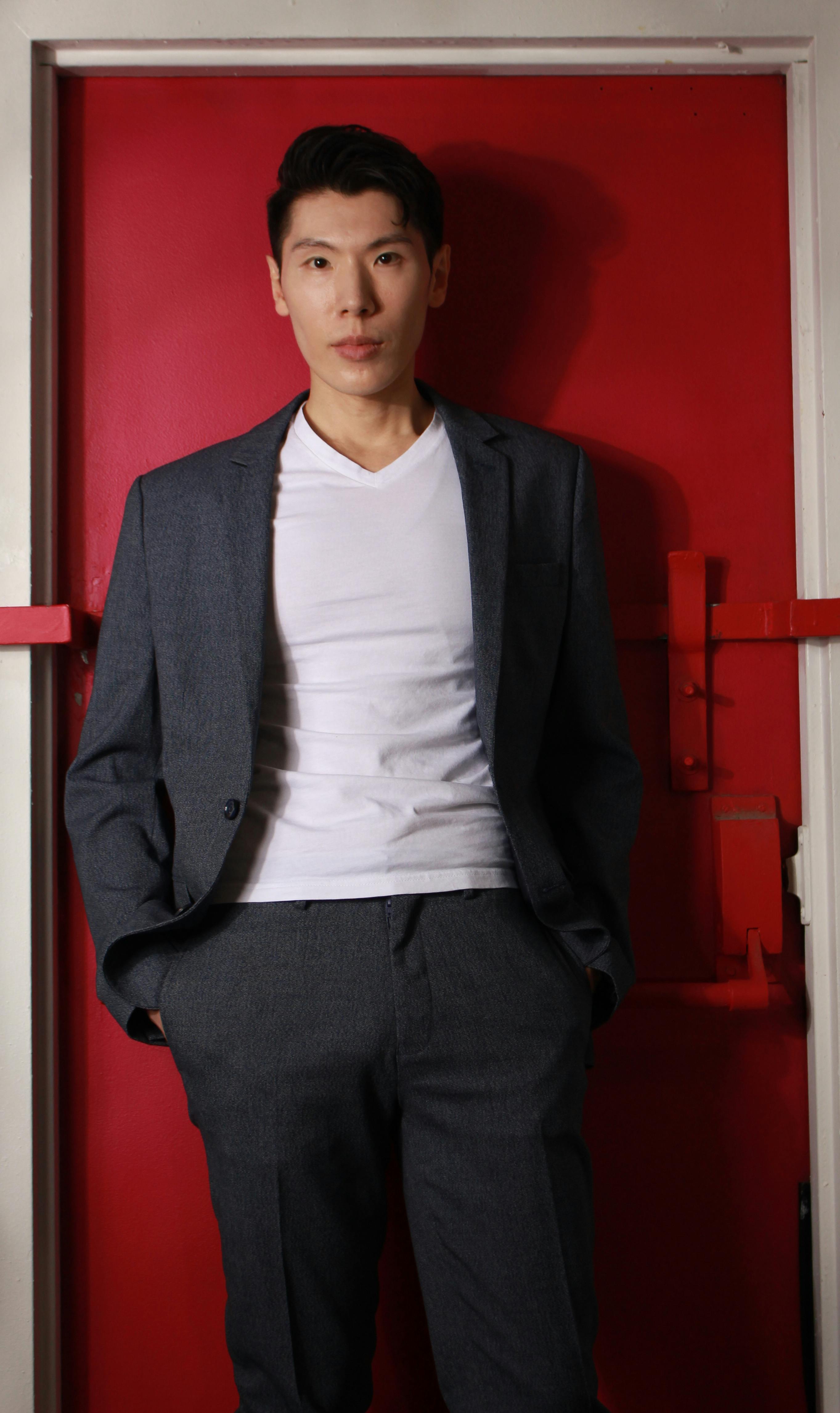 Confident man in a gray suit with a white shirt, posing indoors against a vibrant red background.