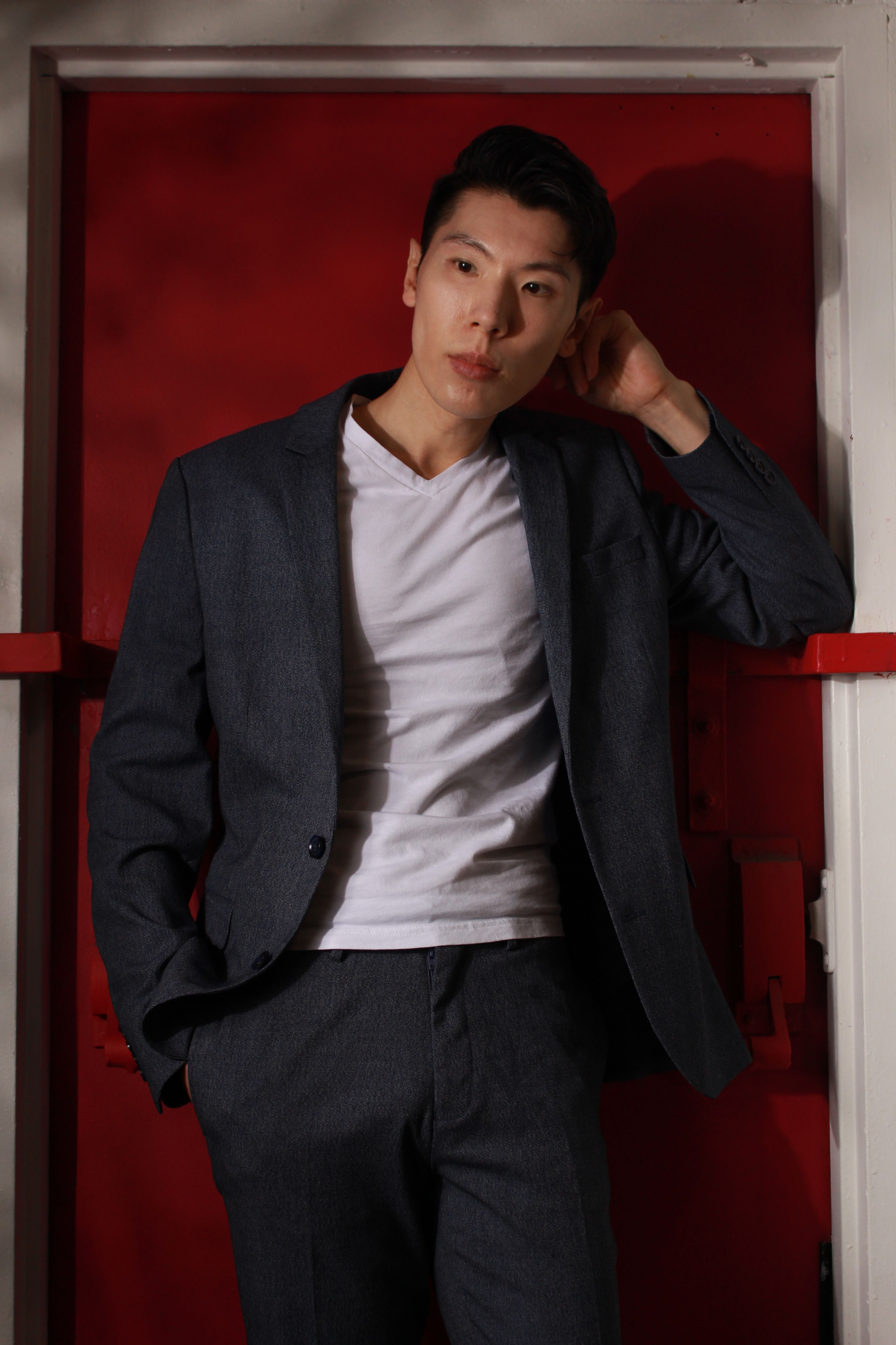 Elegantly dressed man posing against a vibrant red door indoors, emphasizing modern style.