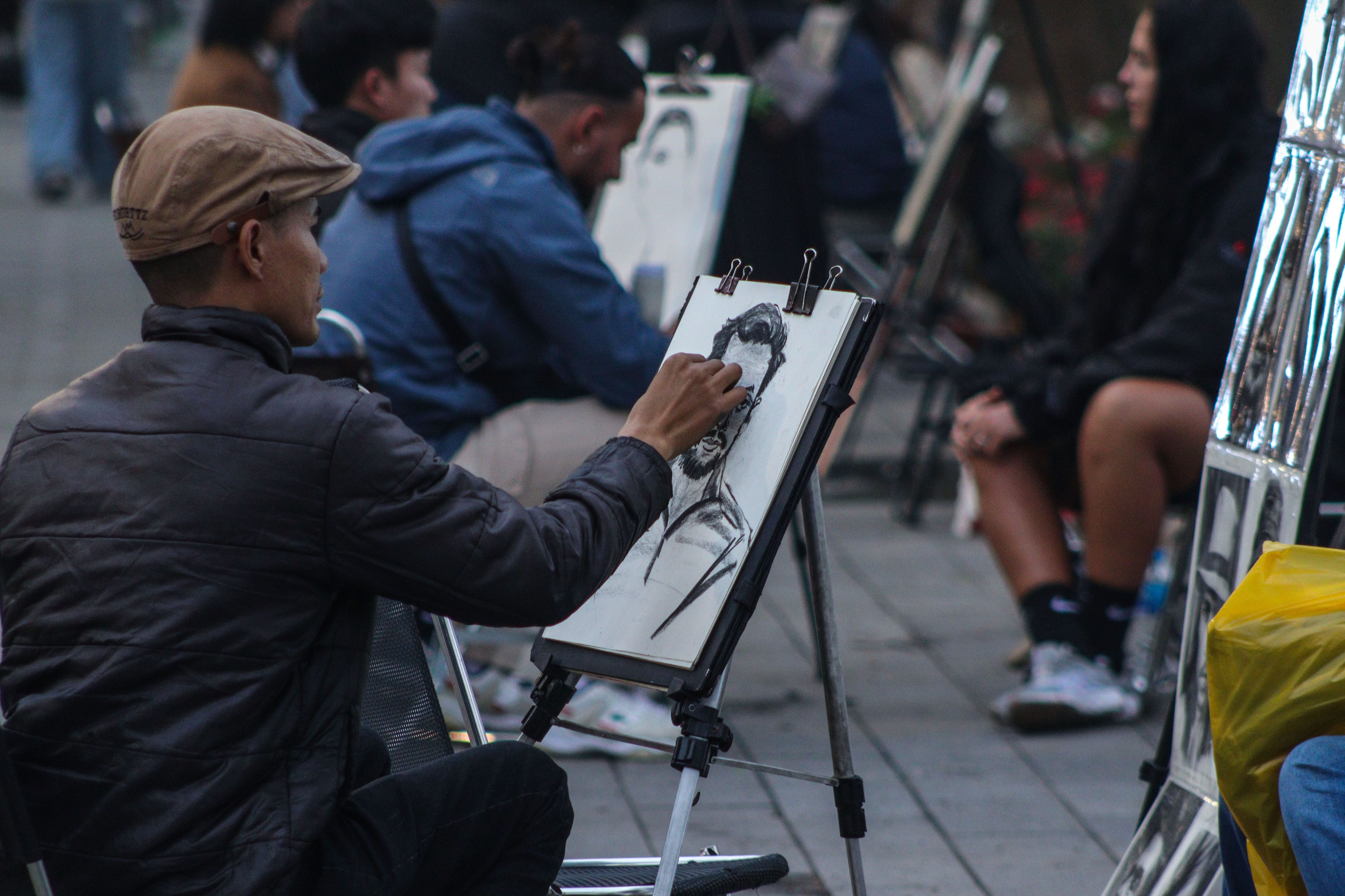 A street artist creates a detailed charcoal portrait sketch outdoors with surrounding onlookers.