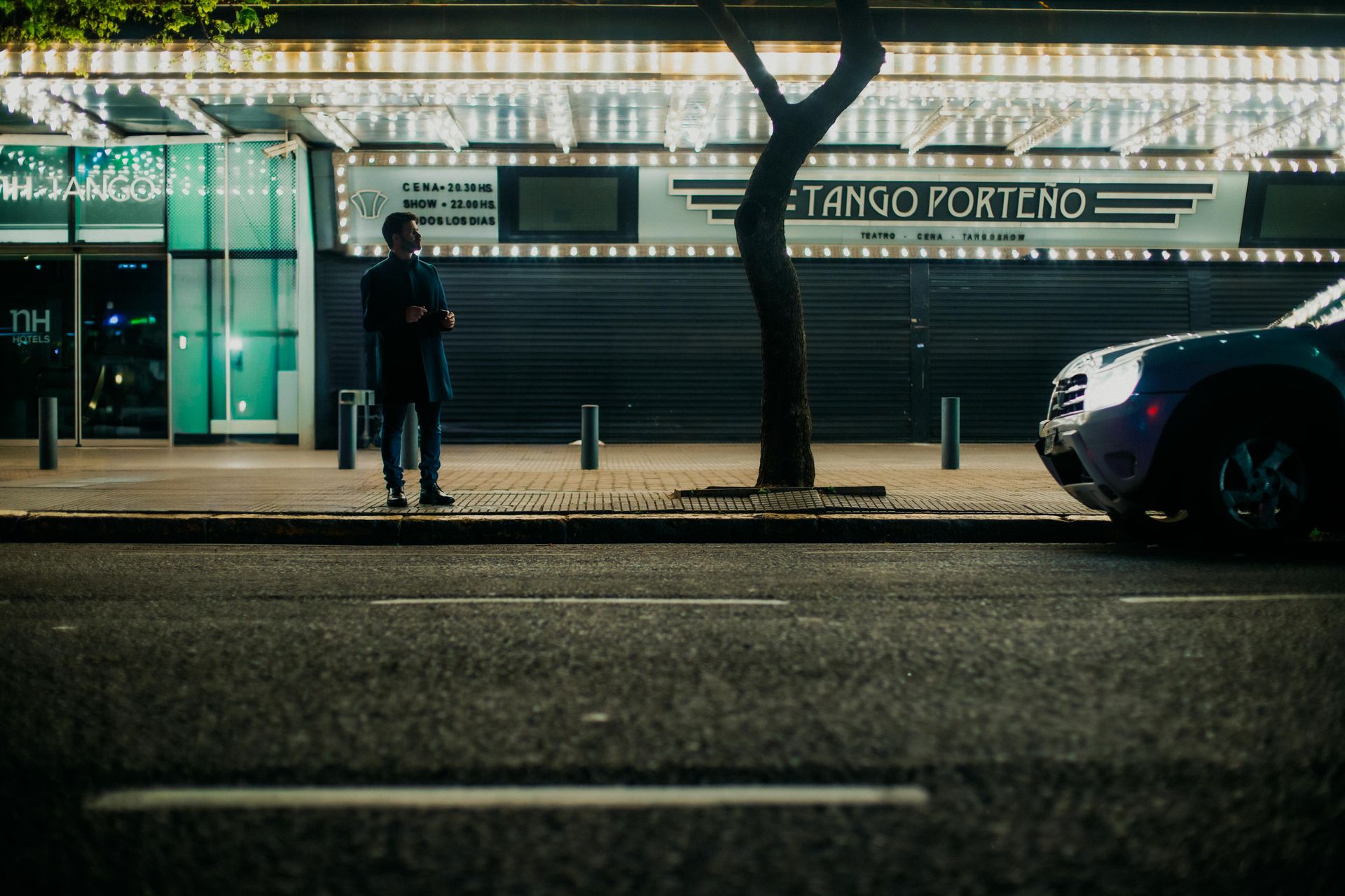 A stylish urban night scene featuring a man standing near Tango Porteño in Buenos Aires.
