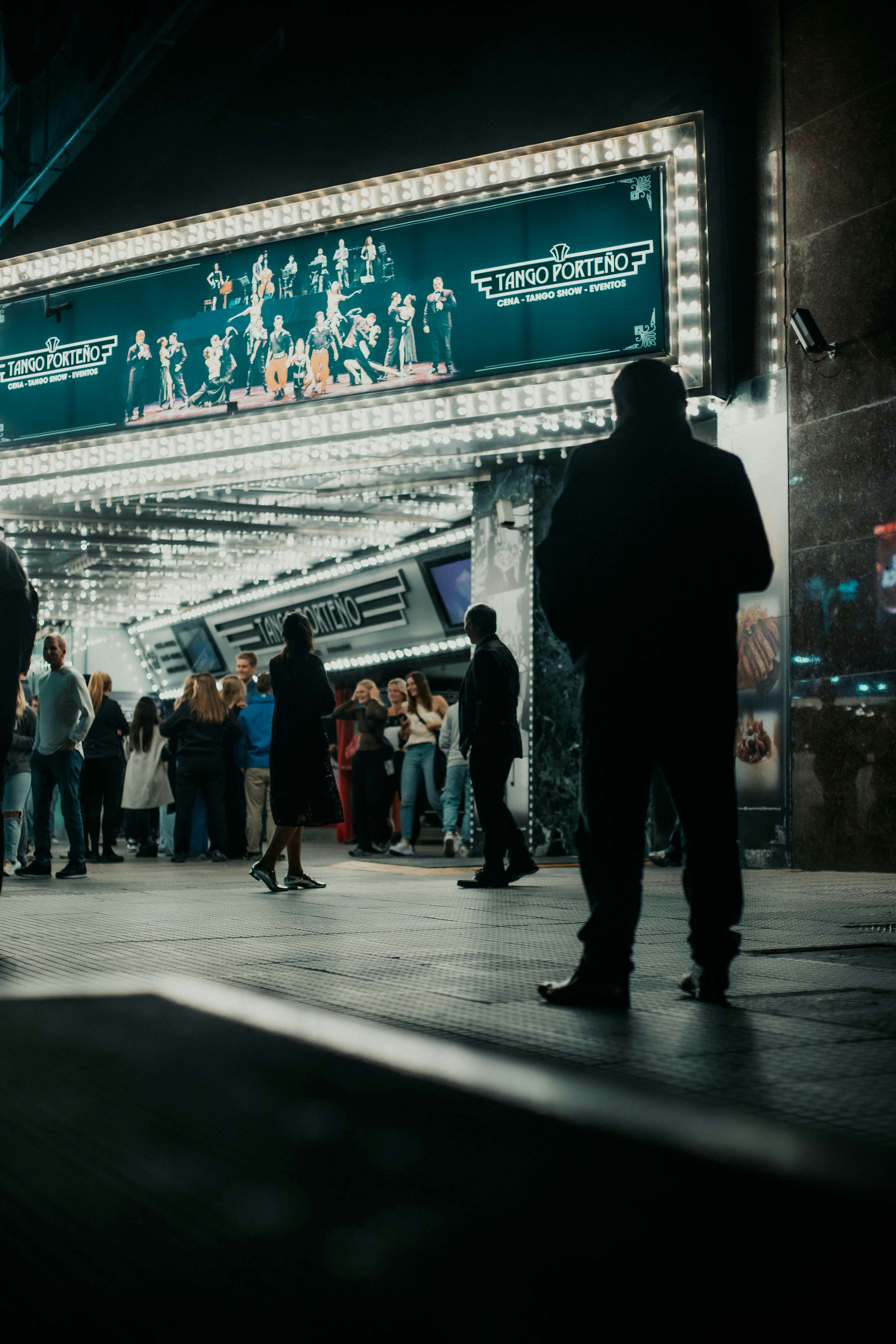 Bezpłatne Tłum zbiera się nocą przed teatrem, pod jasnymi światłami, co tworzy ożywioną, miejską atmosferę. Zdjęcie z galerii