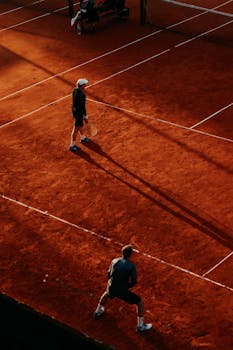 Shot of two tennis players on a clay court during sunset from an elevated angle.