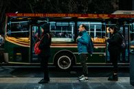 Commuters line up at night in Buenos Aires, waiting beside a colorful city bus.