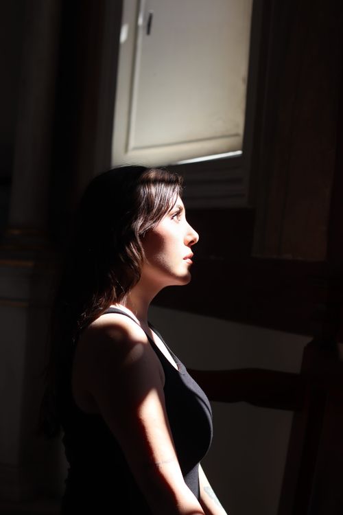 Free A woman in profile sits pensively in soft window light, creating dramatic shadows. Stock Photo