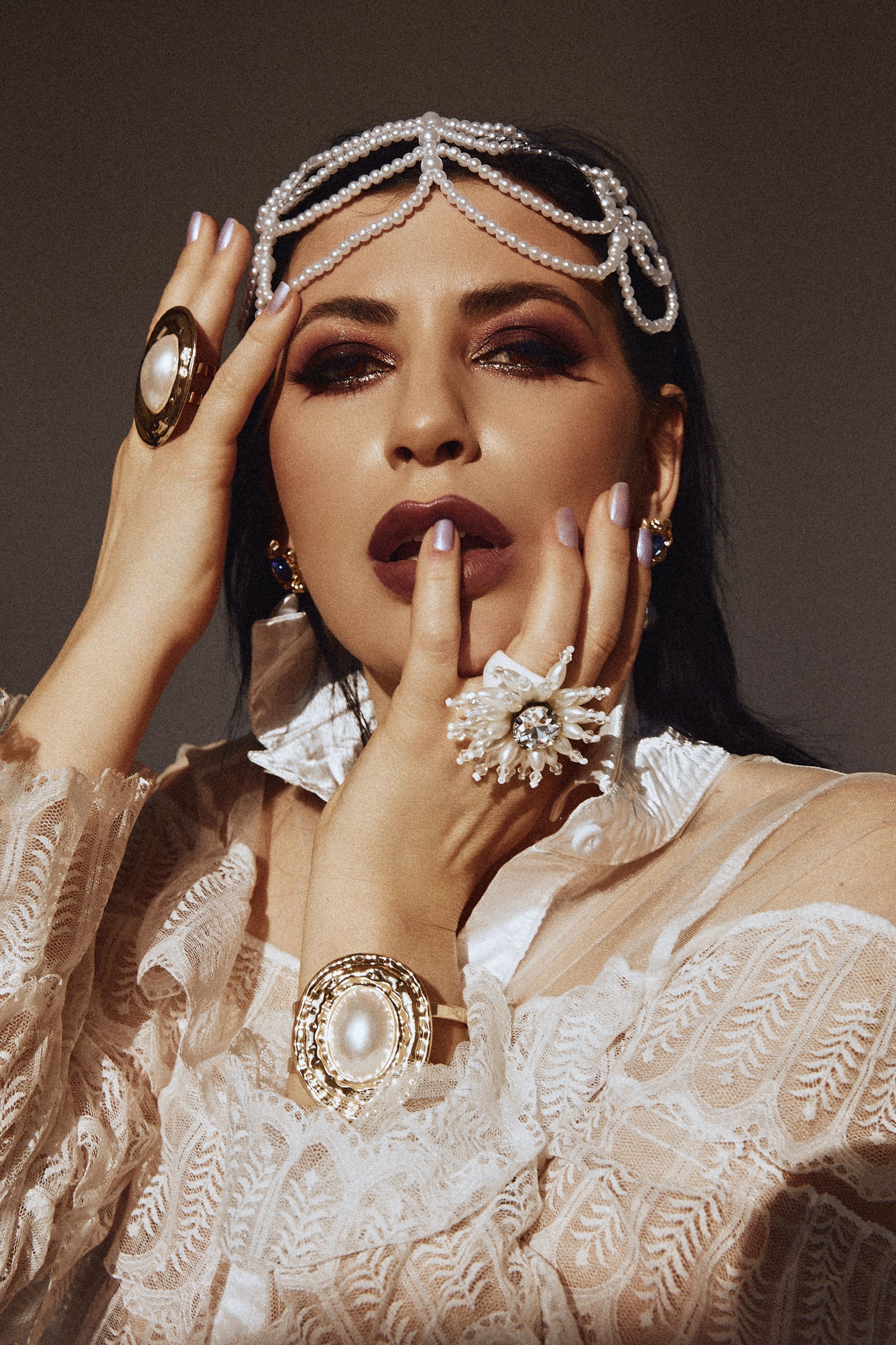 Elegant woman poses with pearl jewelry and vintage attire, exuding grace and style.
