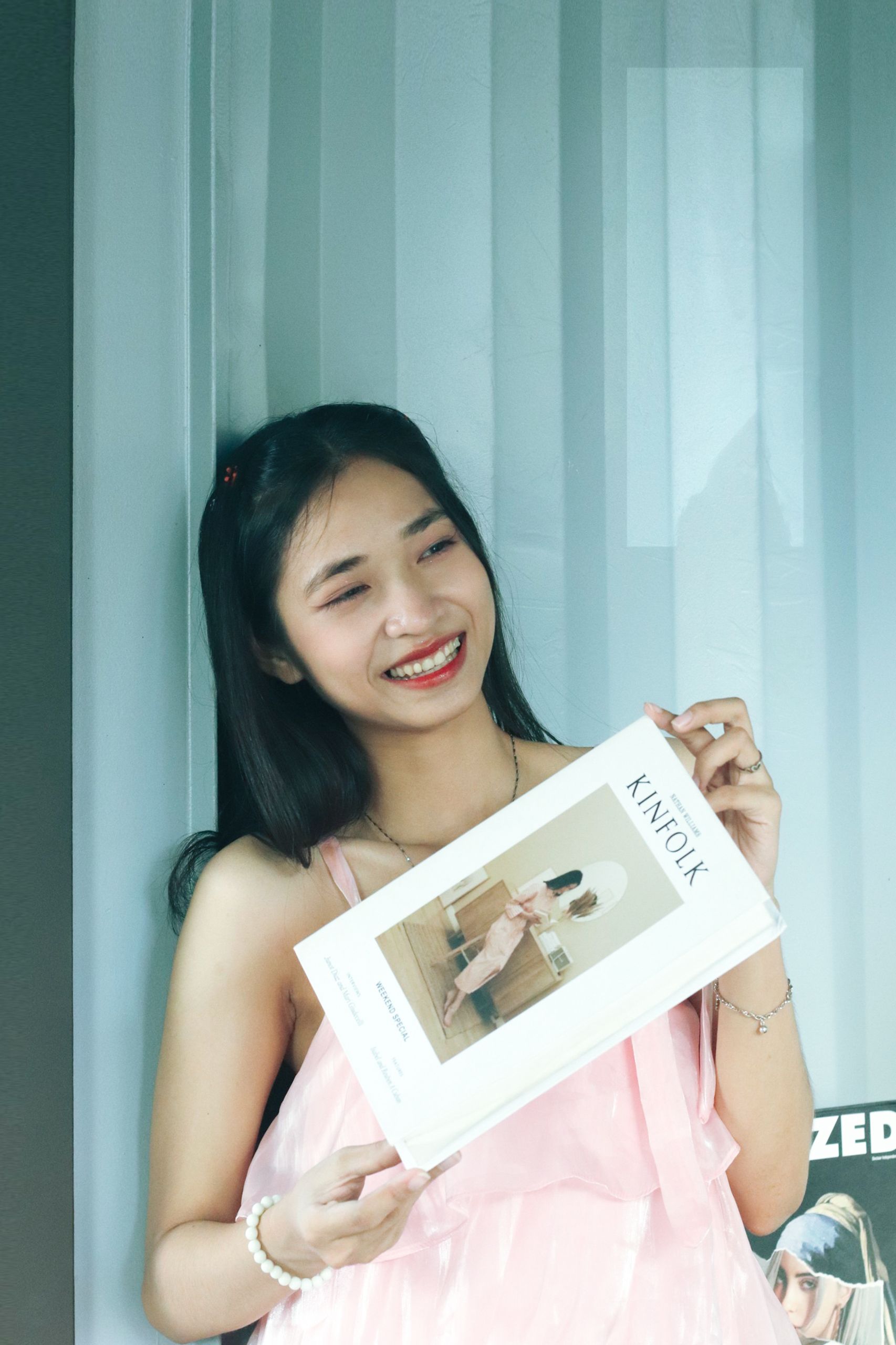 Smiling young woman holding a Kinfolk magazine indoors with natural light.
