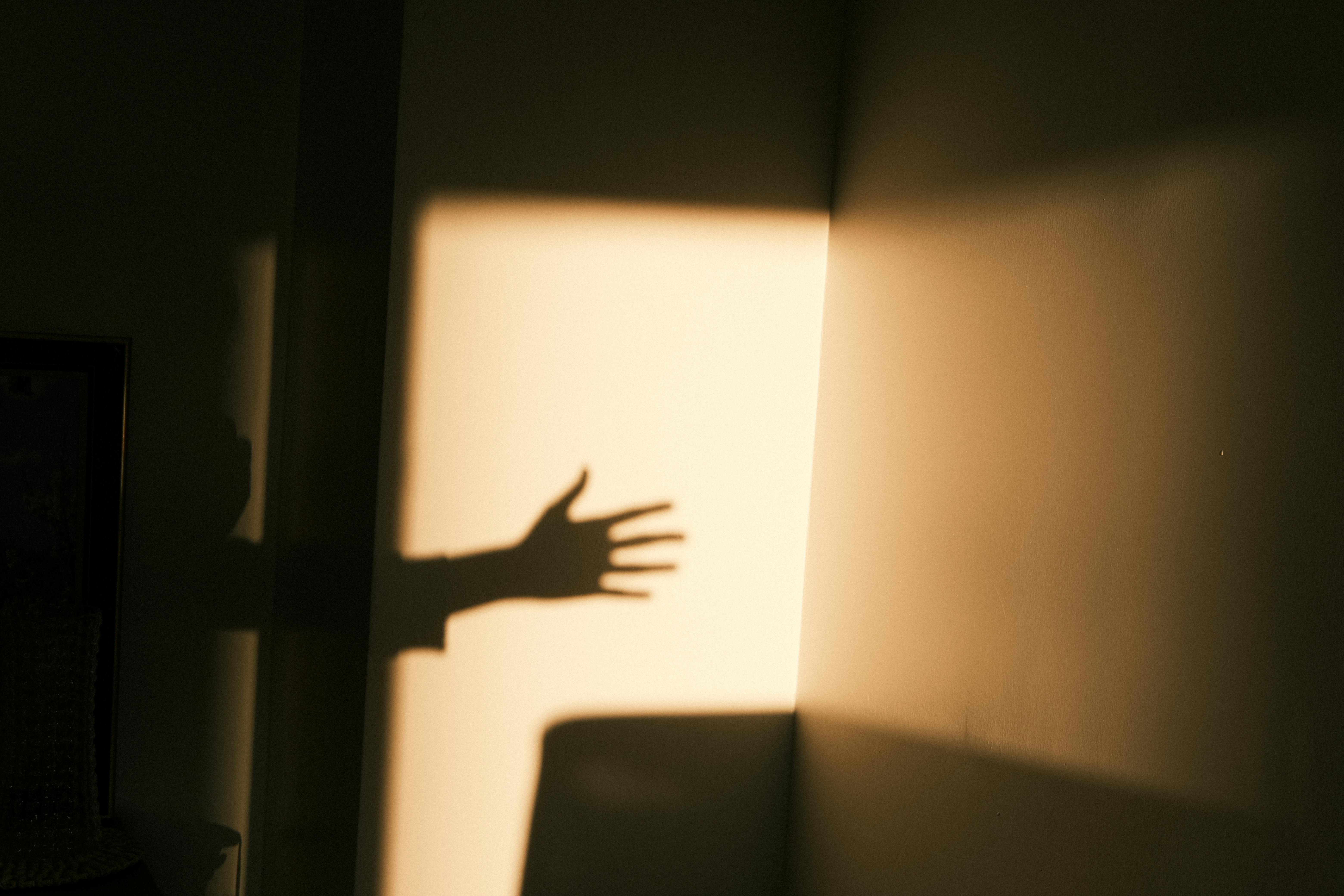 A dramatic shadow of an outstretched hand cast on a wall at sunset, evoking mystery.