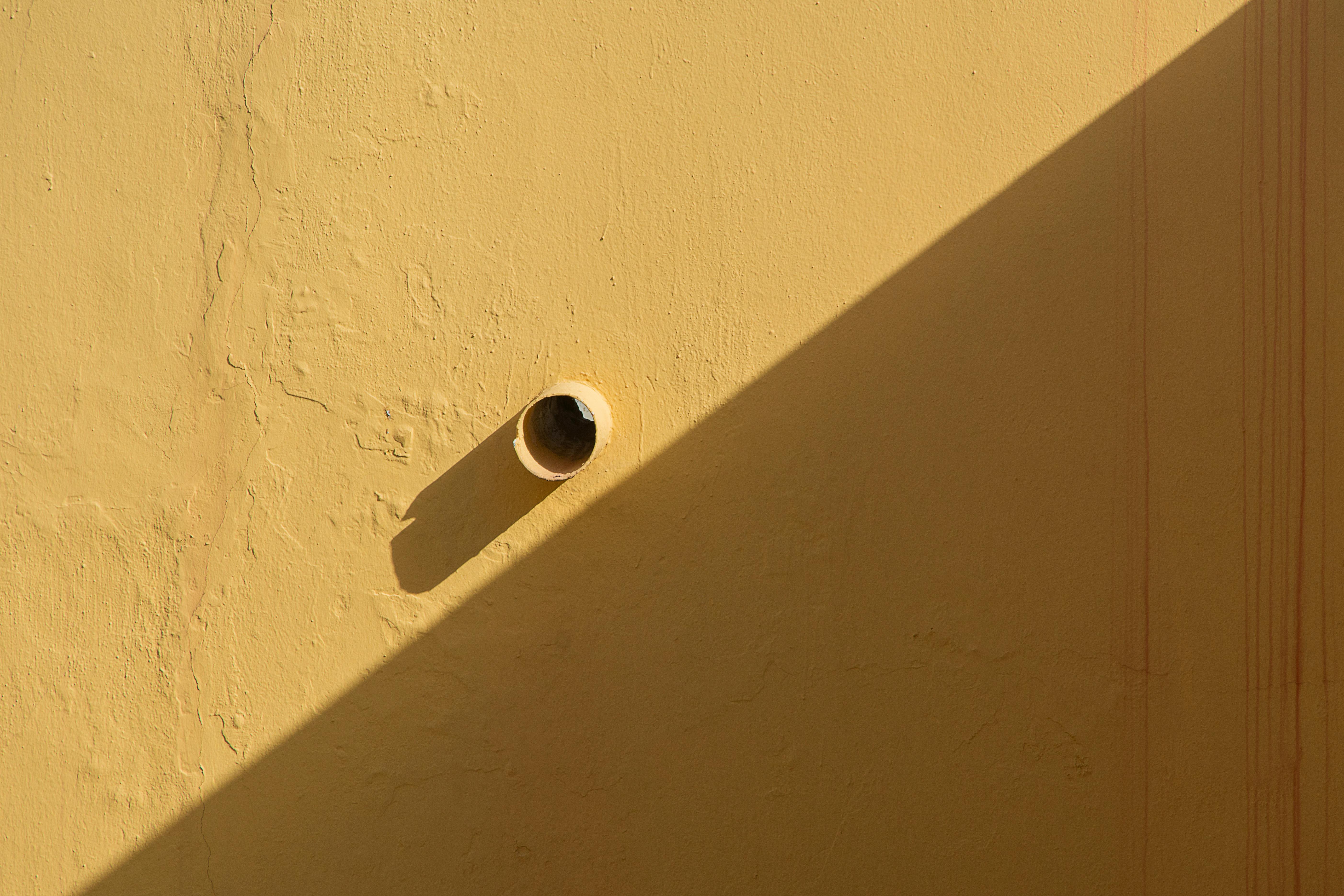 bezplatná Žlutá stěna s vyčnívající trubkou a silným geometrickým stínem v přirozeném světle. Základová fotografie