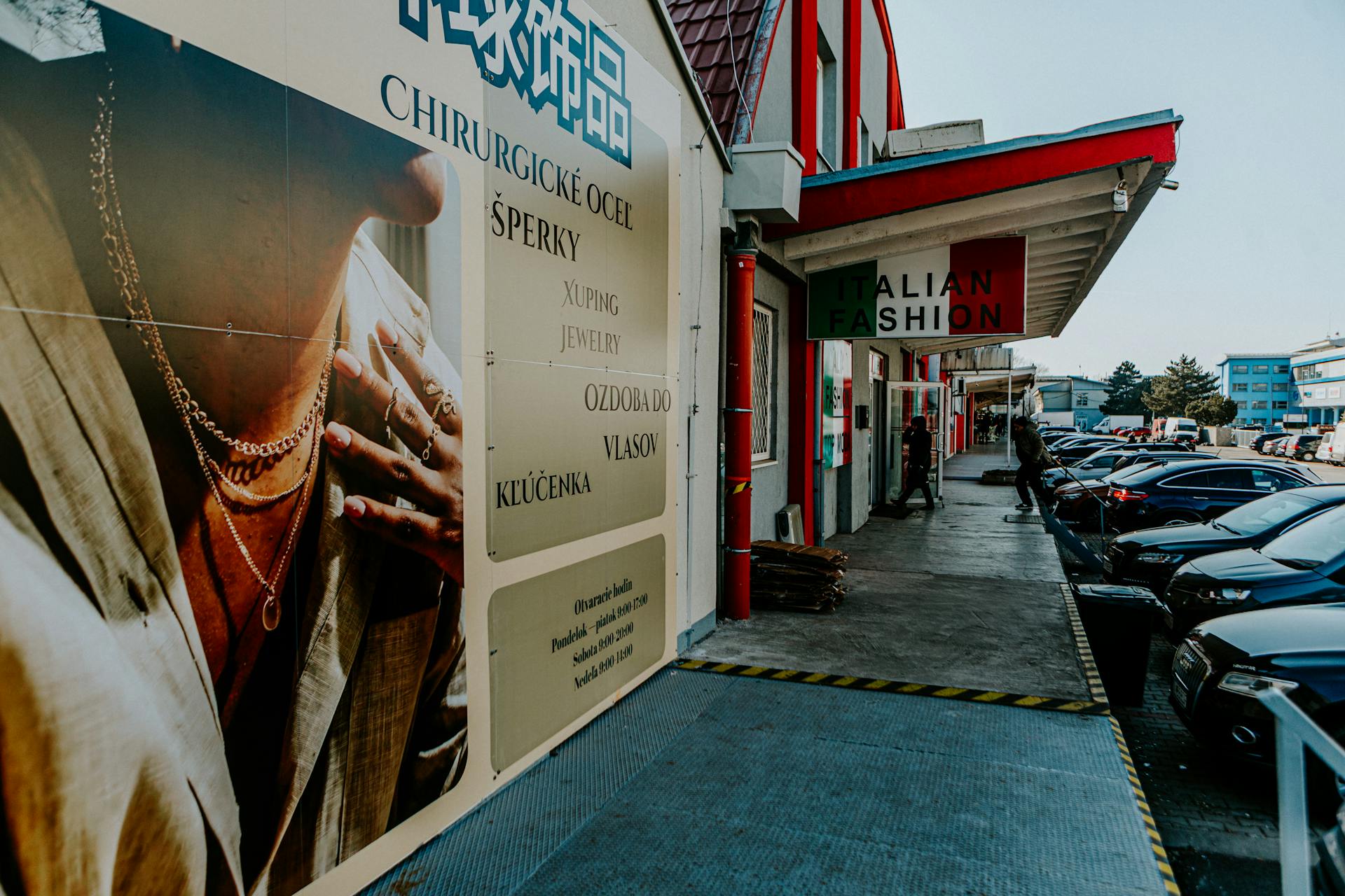 Outdoor view of fashion stores and advertising poster with parked cars and pedestrians.