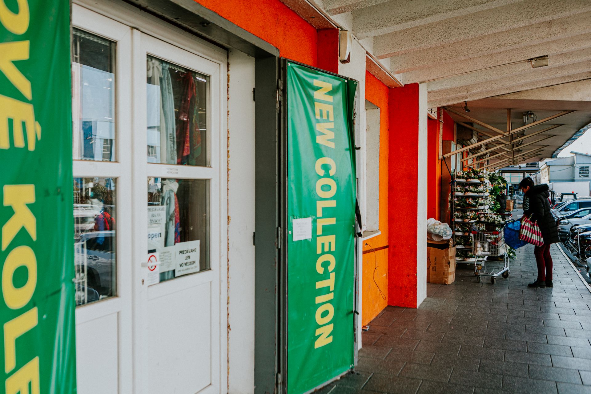 Street scene featuring a storefront with new collection signage and a person walking by.
