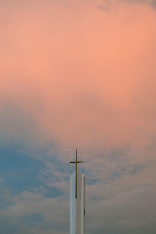 Free A church spire with a cross silhouetted against a vibrant sunset sky, reflecting tranquility. Stock Photo