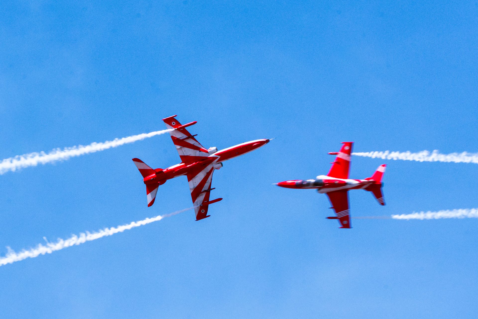 Two red fighter jets performing aerial acrobatics in the clear Bengaluru sky.