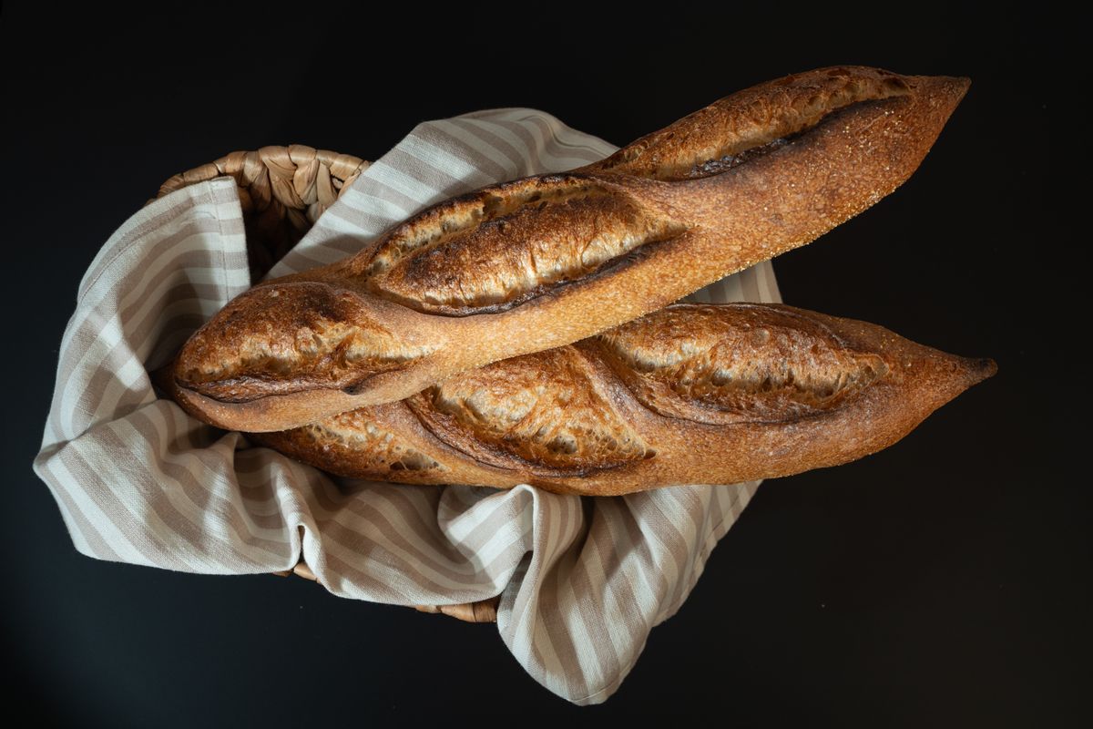 Two dark-crusted scored baguettes resting on a striped linen cloth against a black background
