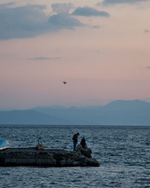 Free Couple enjoying a serene evening by the sea at sunset. Stock Photo
