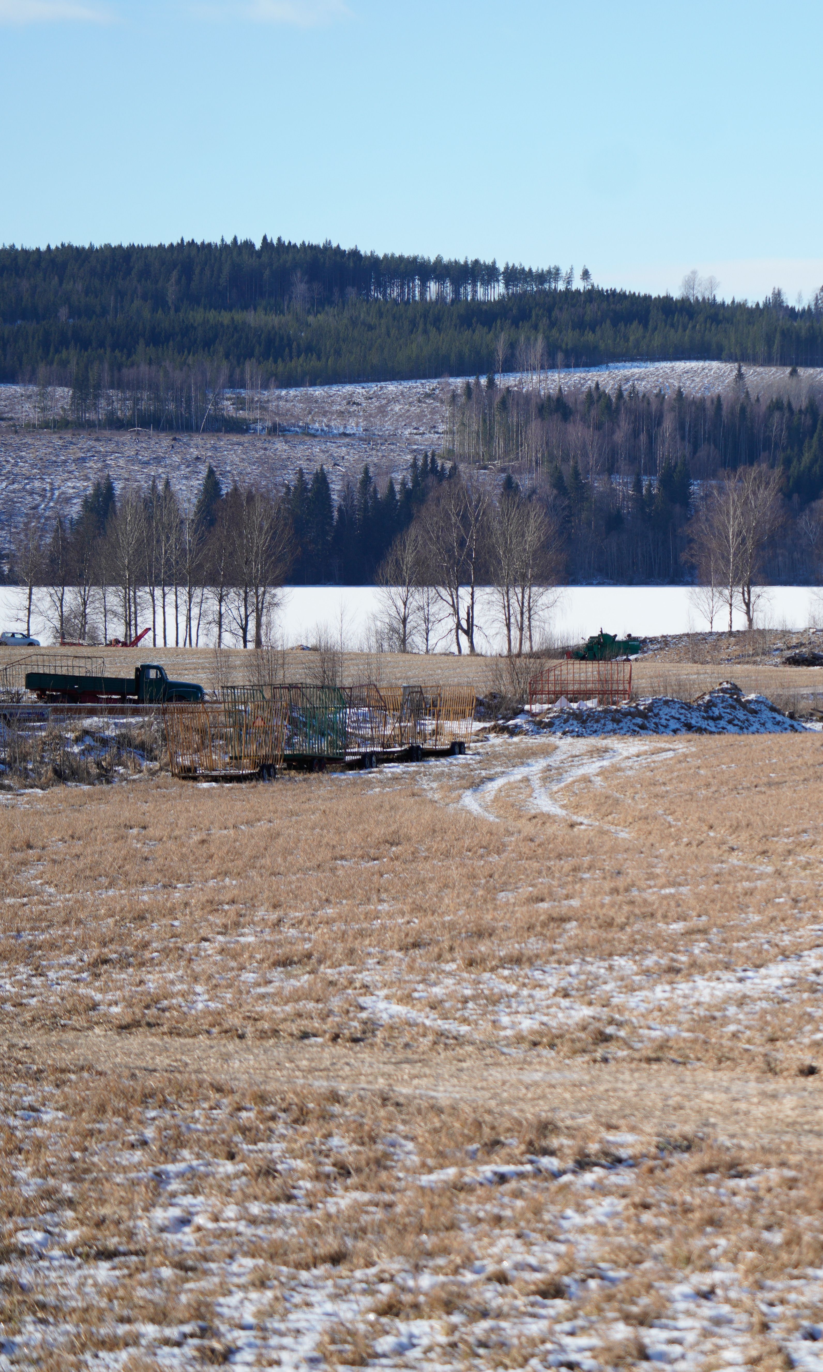 A winter view of a frosty farmland surrounded by forested hills under clear blue skies.