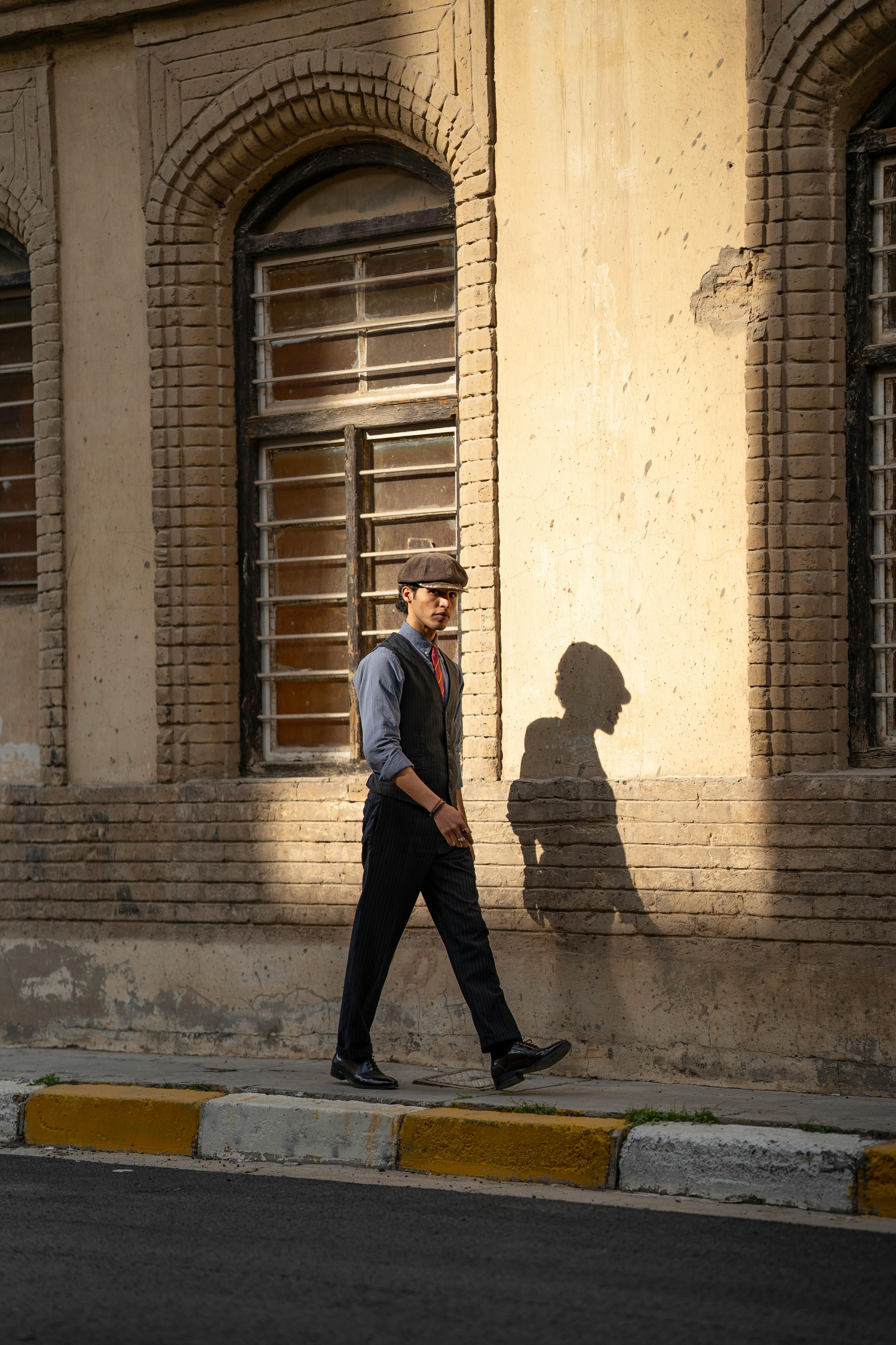Man in hat walks by brick wall, casting shadow in golden sunset light.
