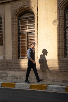 Man in hat walks by brick wall, casting shadow in golden sunset light.