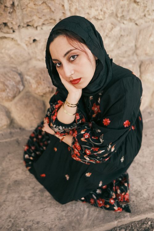 Free Contemplative woman in floral dress leans against a textured wall, exuding elegance. Stock Photo