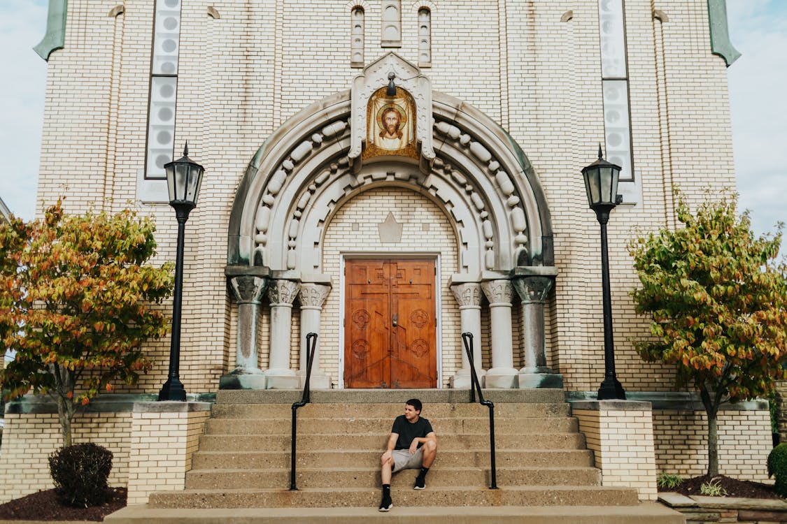 Man Wearing Black Crew-neck Shirt Sitting in Front of Church