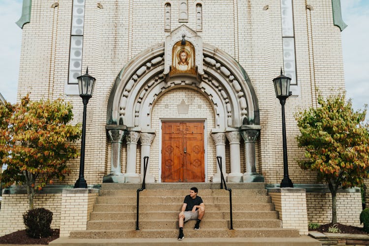 Man Wearing Black Crew-neck Shirt Sitting In Front Of Church