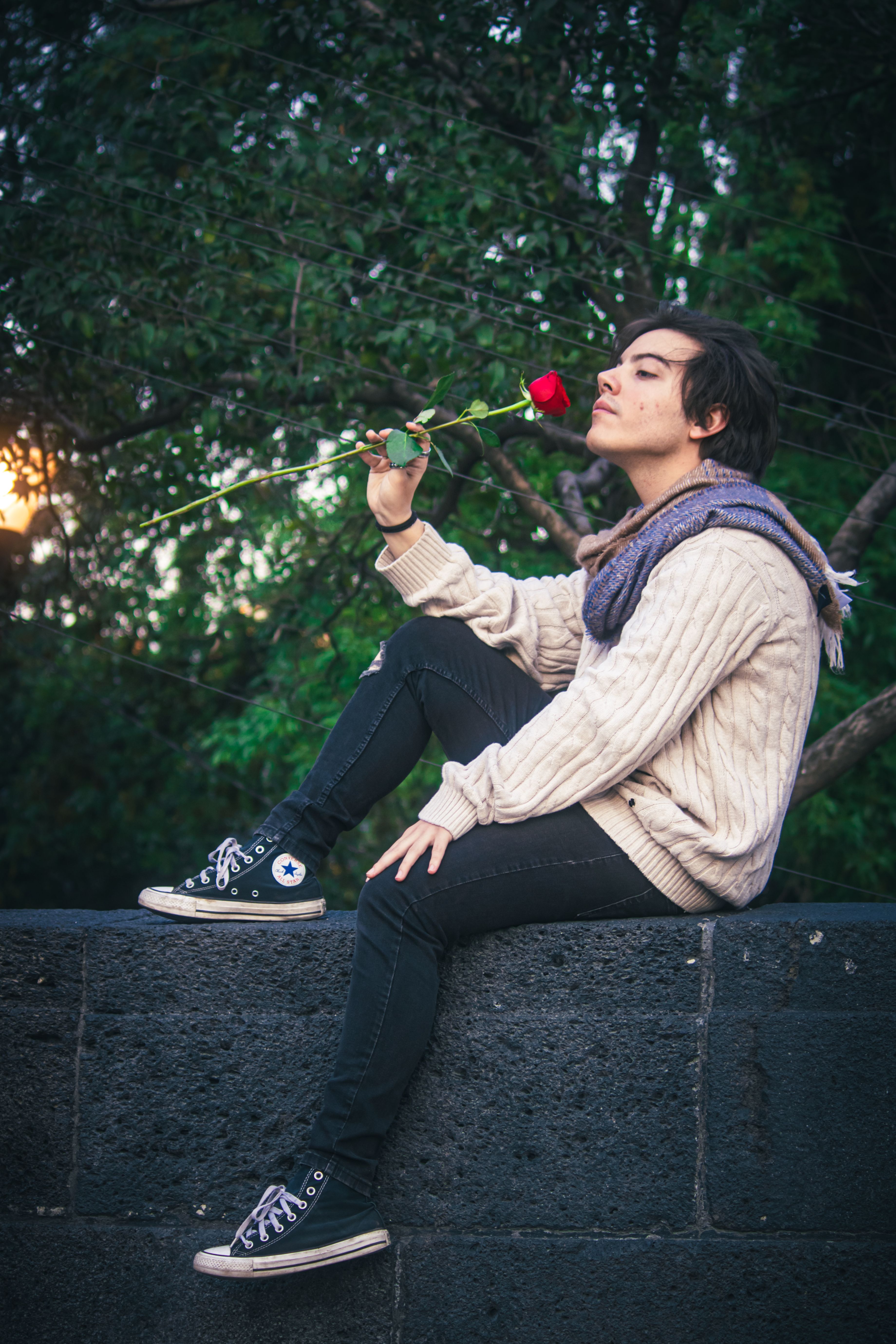 A young man smelling a red rose in a romantic park setting during sunset.