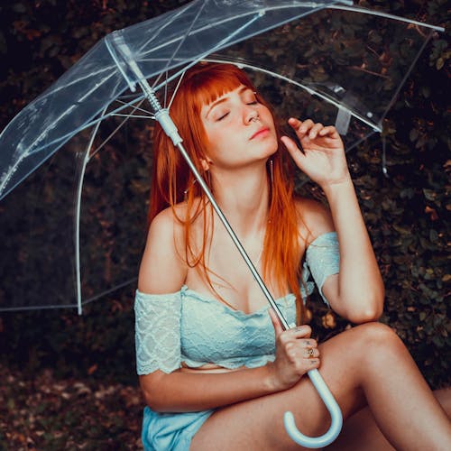Photo of Woman Sitting While Holding a Clear Umbrella With Her Eyes Closed