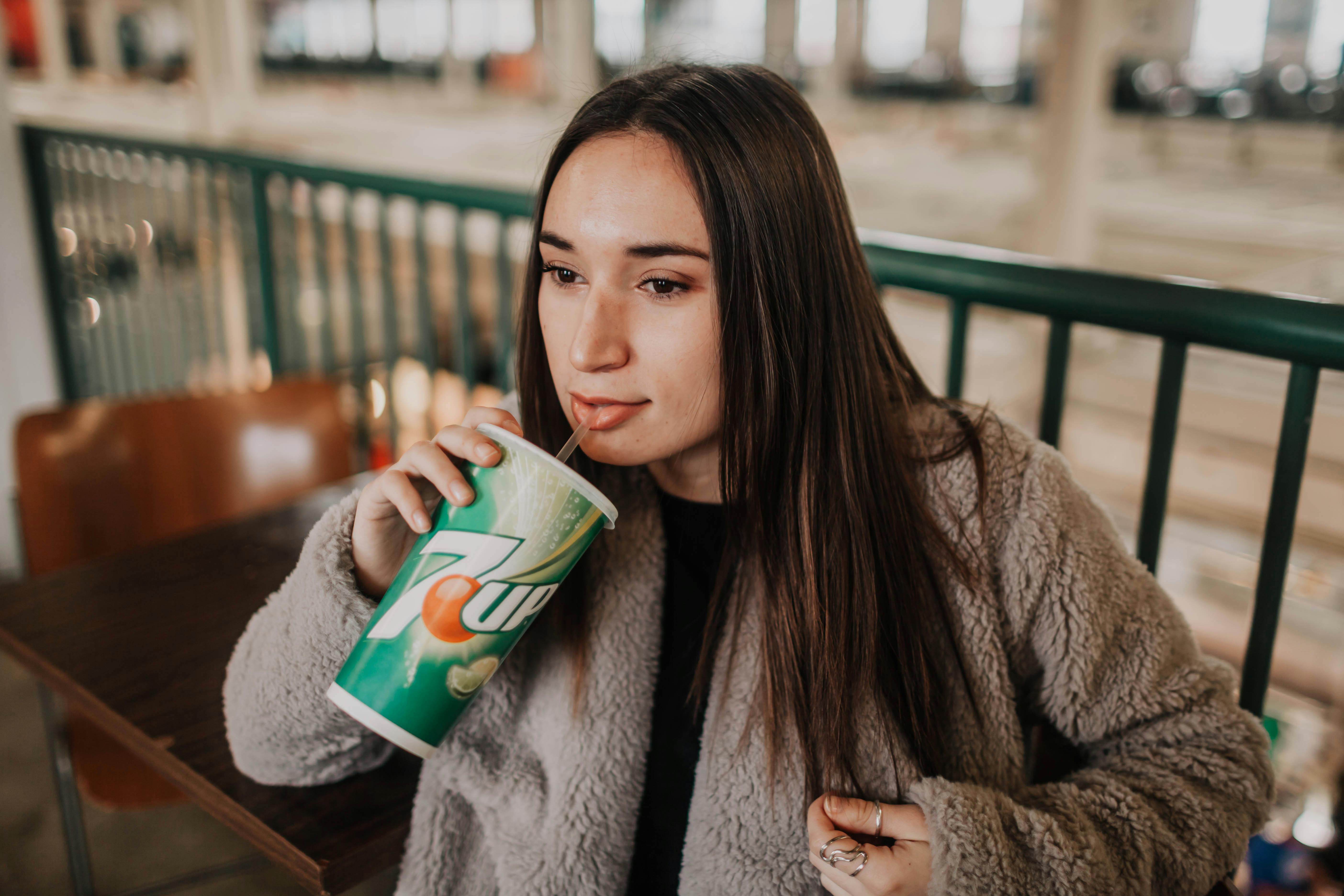 A young woman enjoying a 7UP soda in an indoor setting, creating a relaxed atmosphere.