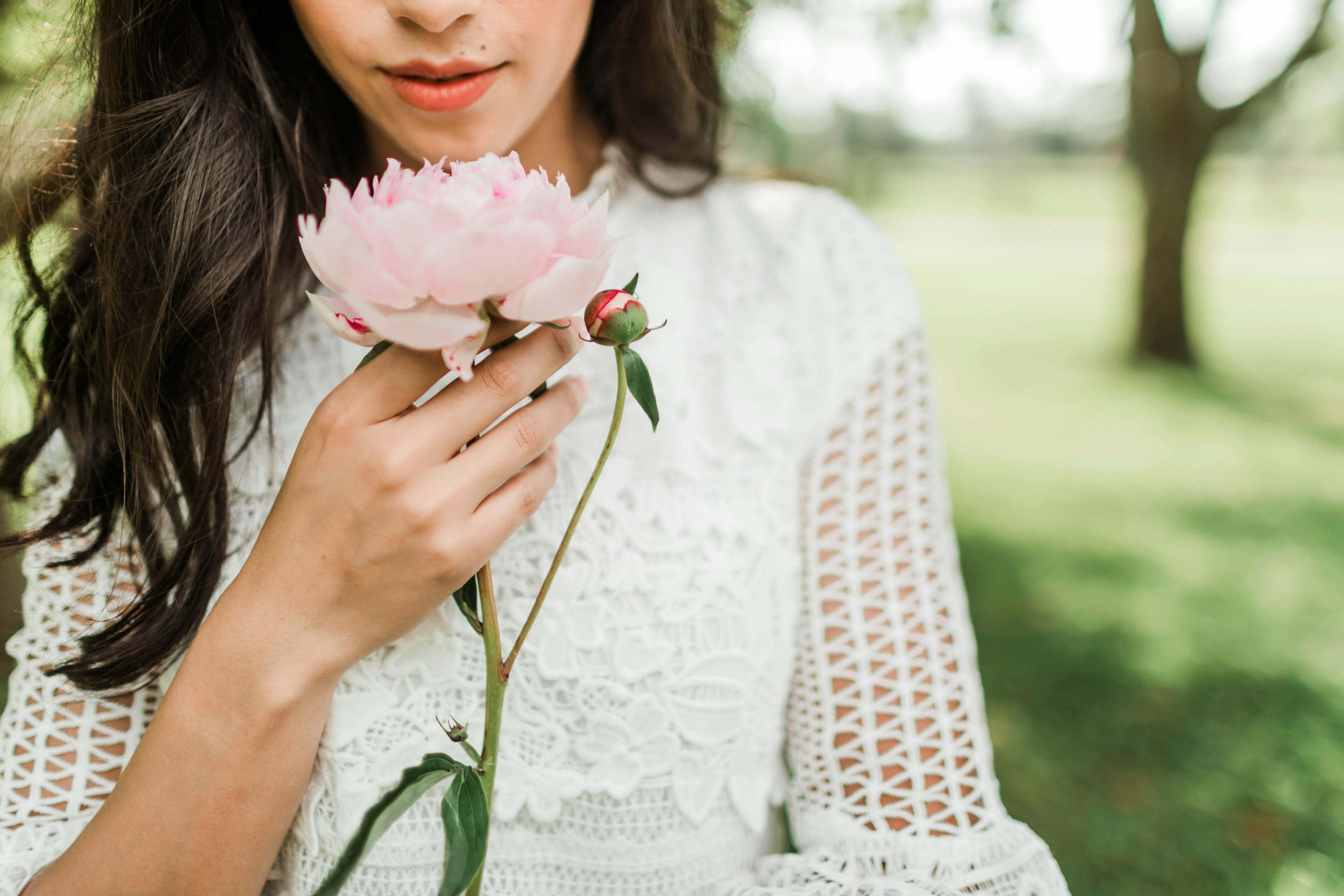 Close-up of a woman holding a pink peony in an outdoor setting, emphasizing floral elegance.