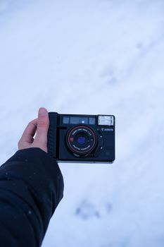 Hand holding vintage camera against snowy background, conveying a nostalgic winter feel.