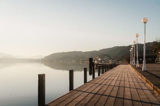 Peaceful morning view of a lakefront promenade with distant mountains and clear skies.