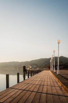 A peaceful lakeside boardwalk at sunrise with reflections and mountain views.