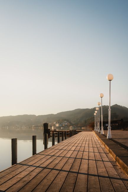 A peaceful lakeside boardwalk at sunrise with reflections and mountain views.