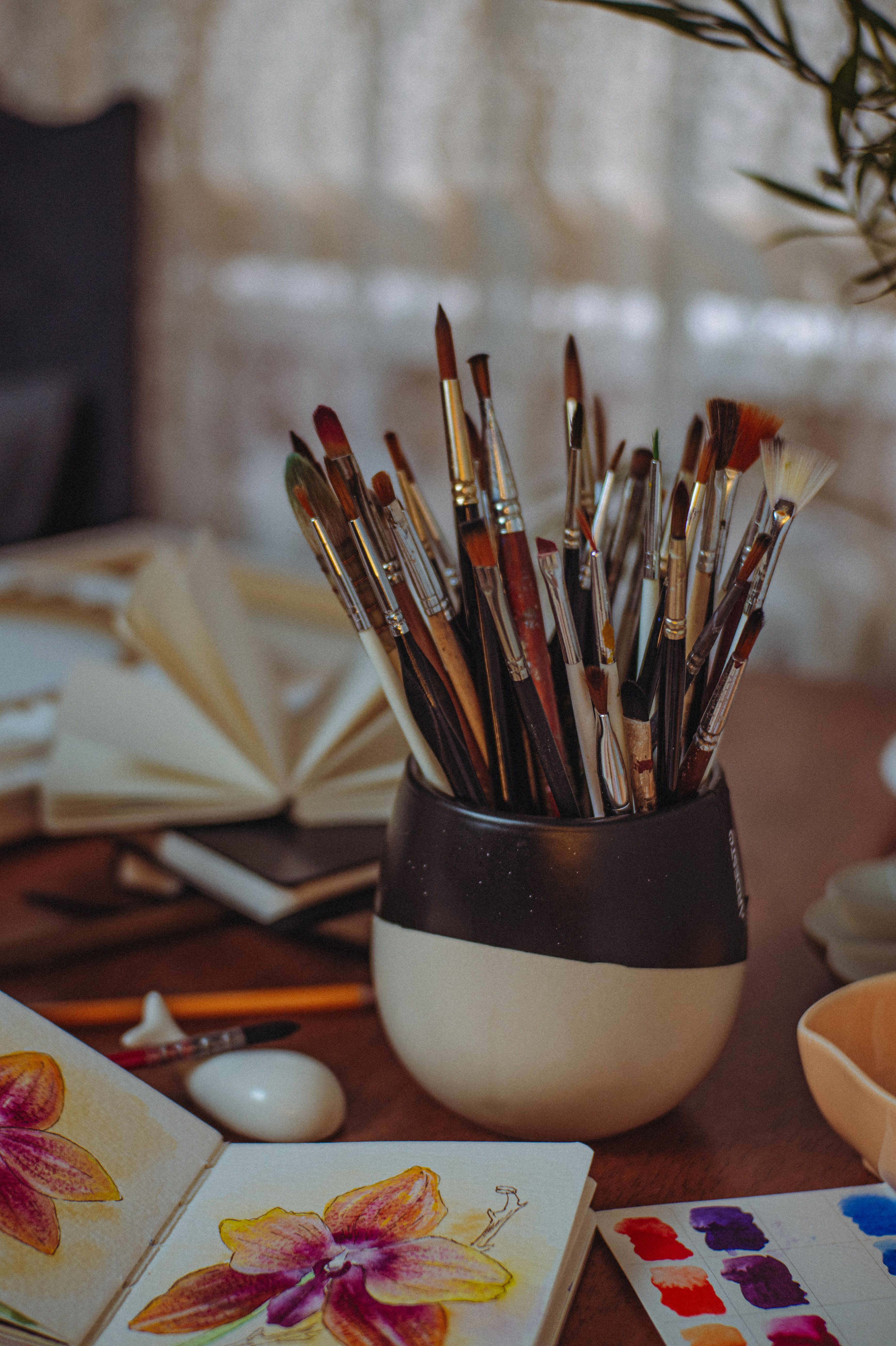 Cozy artistic workspace featuring a collection of paintbrushes, sketchbooks, and watercolor palettes.