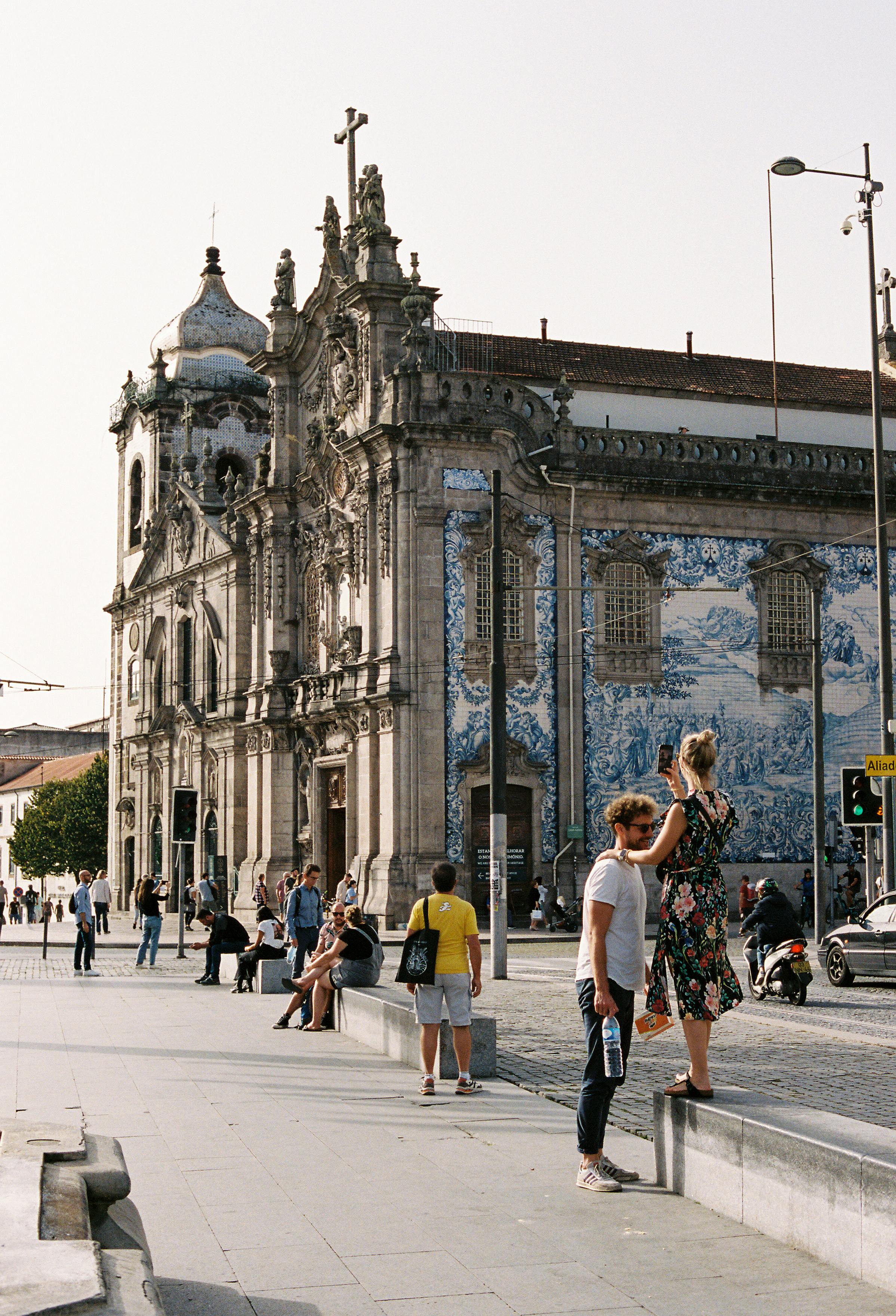 Visitors gather around the iconic tiled Igreja do Carmo in Porto, enjoying the sunny atmosphere.