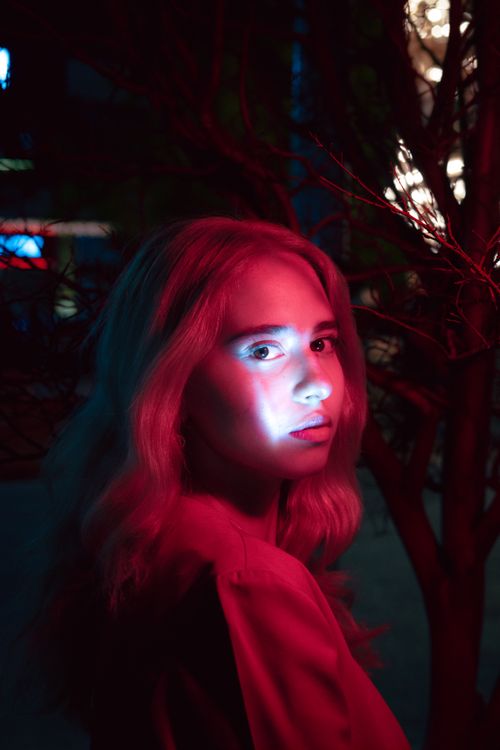 Free A person illuminated by vibrant neon lights in a mysterious outdoor setting. Stock Photo
