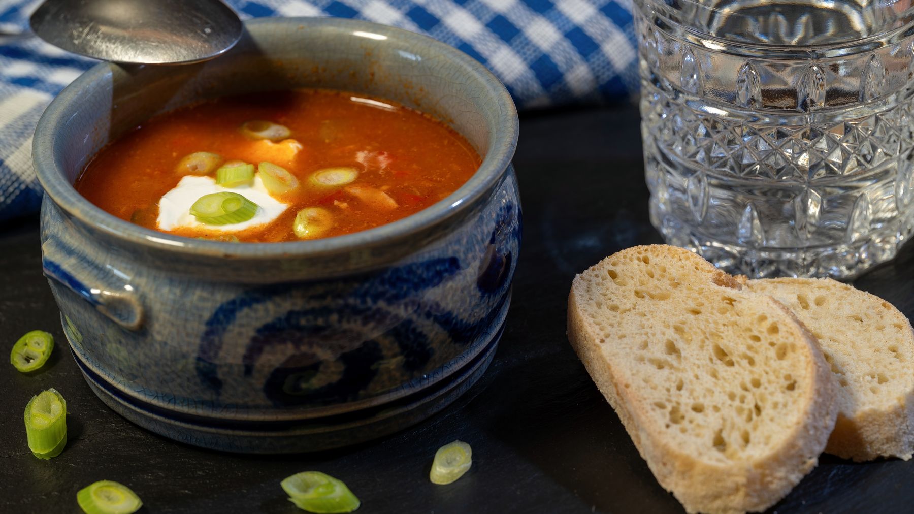Cozy bowl of solyanka soup served with sour cream, sliced bread, and herbs.