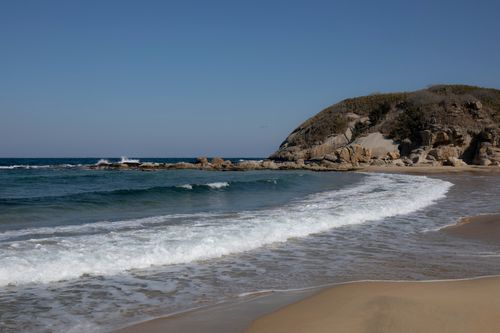 Free Peaceful beach scene with waves lapping at rocky shore under clear blue sky. Stock Photo