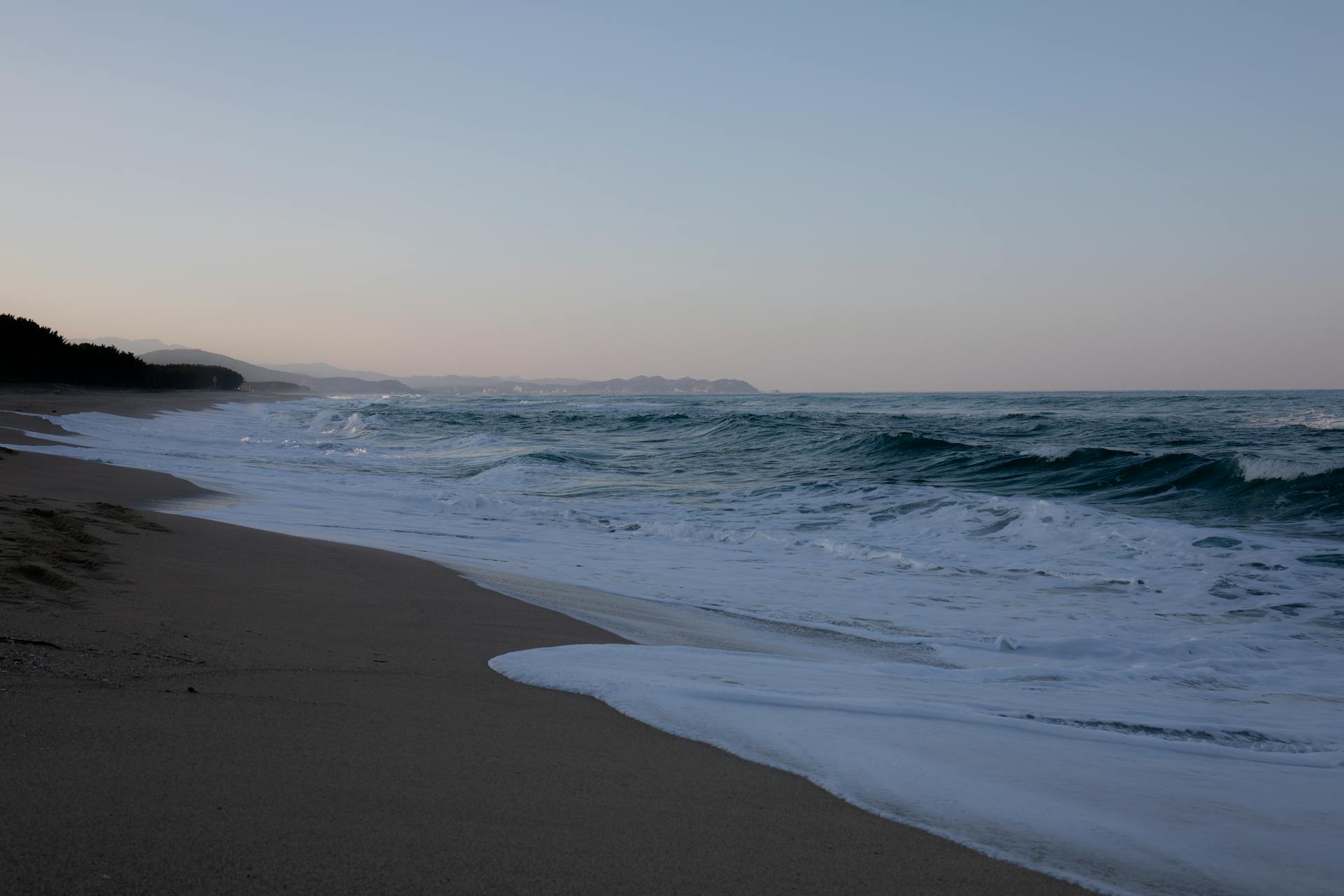 Peaceful sandy beach with gentle waves at sunrise, creating a tranquil coastal scene.