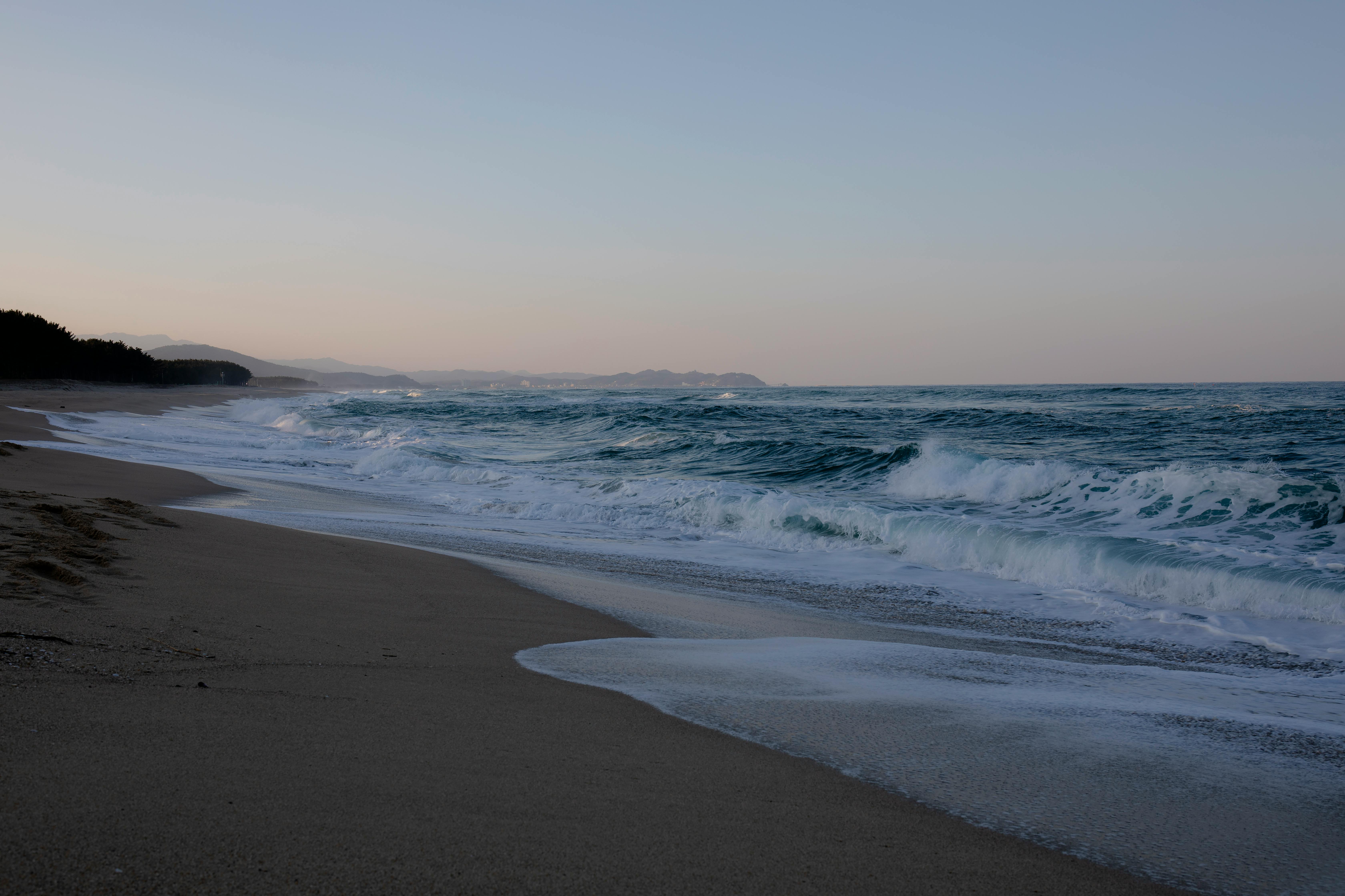 A serene beachscape with gentle waves and a distant view of the horizon at dusk.