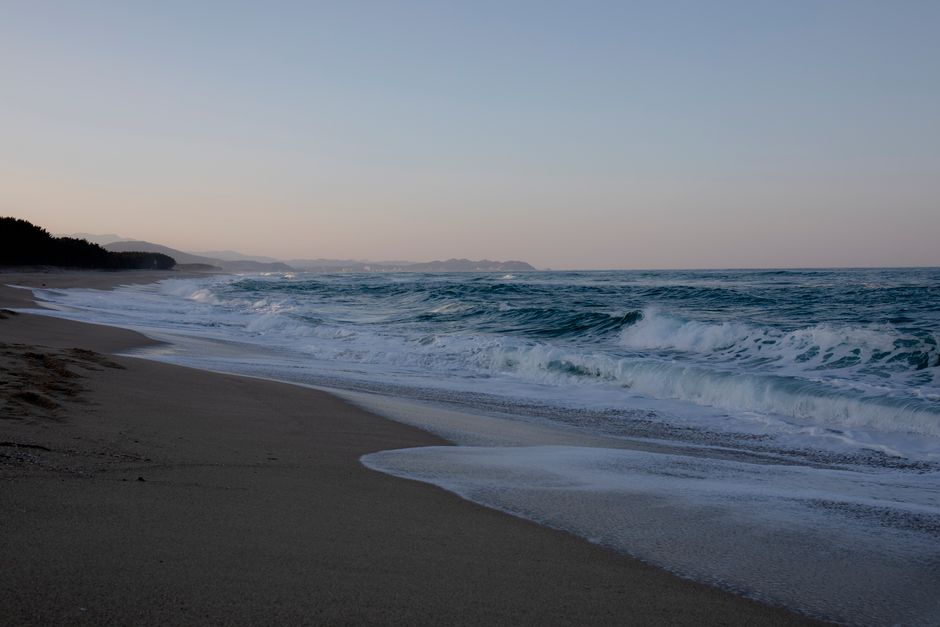 A serene beachscape with gentle waves and a distant view of the horizon at dusk.