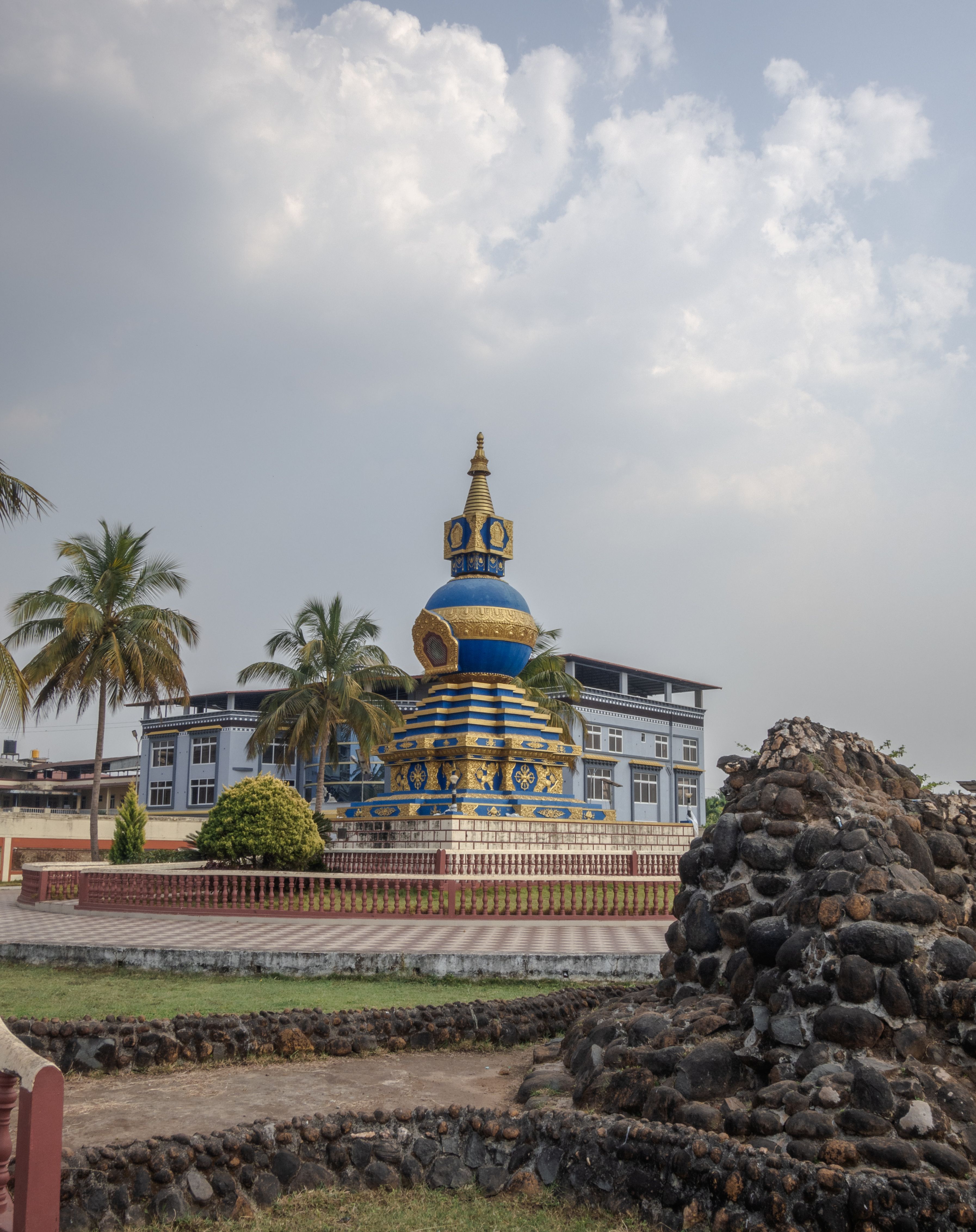 Colorful stupa surrounded by buildings and palm trees in Mundgod, India.